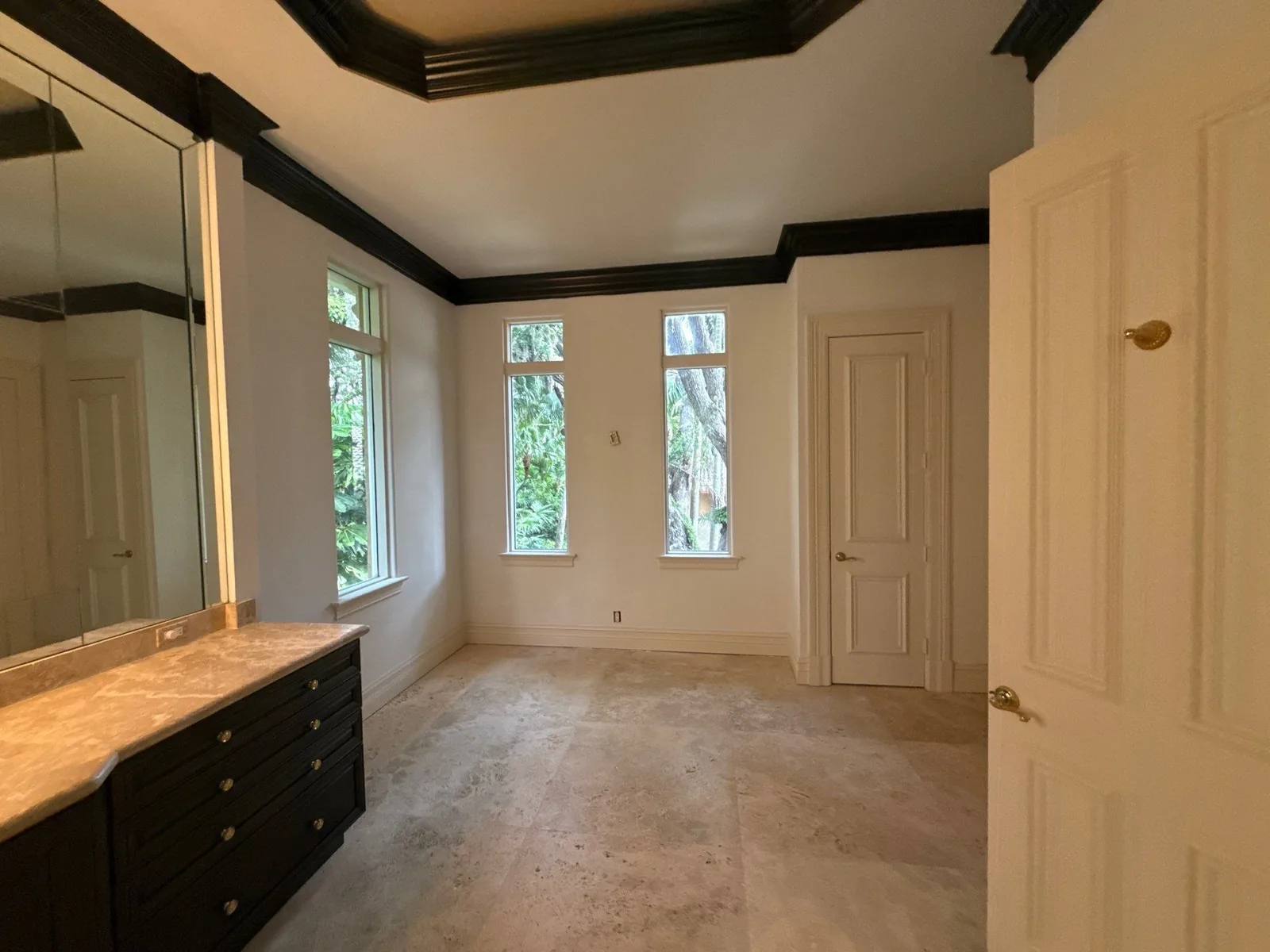 Interior Painting in Jensen Beach, Florida. Empty dressing area with cream walls, dark crown moulding and tray ceiling detail, tall windows and a dark vanity cabinet.