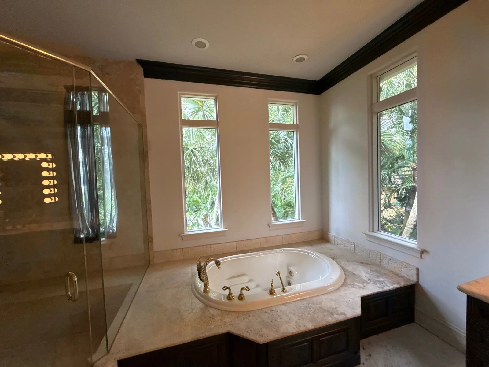 Interior Painting in Jensen Beach, Florida. Master bathroom with painted walls, dark crown moulding, drop-in tub under three windows and a glass shower enclosure.