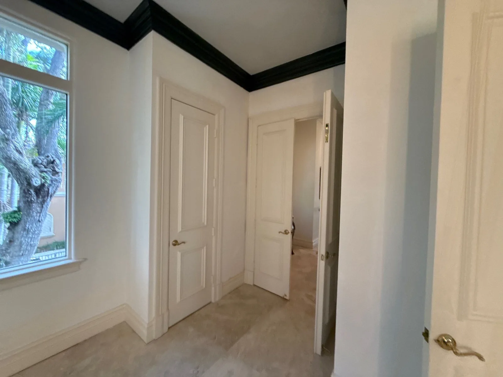 Interior Painting in Jensen Beach, Florida. Hallway with white walls and doors, black crown moulding and light stone tile flooring.