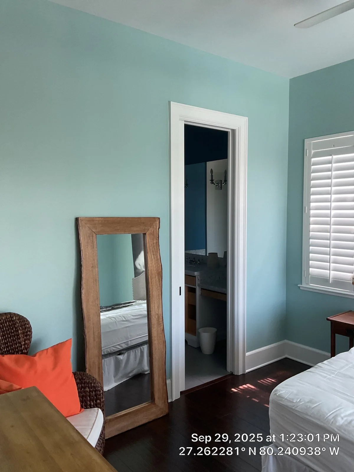 Interior Painting in Jensen Beach, Florida. Bedroom with aqua-green walls and white trim, doorway to an adjoining room, leaning wood-framed floor mirror and plantation-shuttered window.