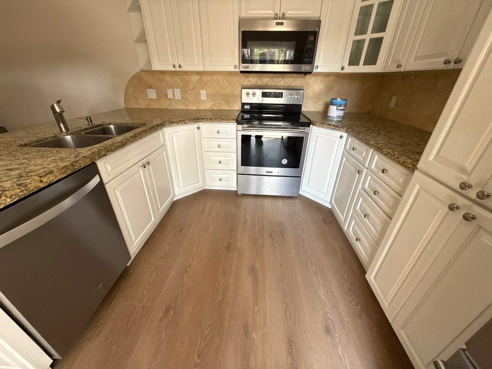 Cabinet Refinishing in Juno Beach, Florida. U-shaped kitchen with cream raised-panel cabinets, tile backsplash, granite counters and stainless range.