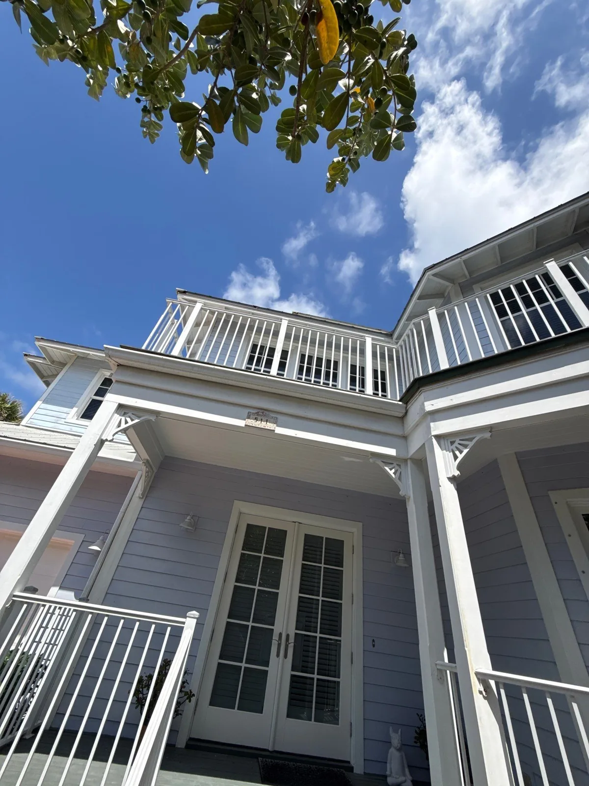 Exterior Painting in Juno Beach, Florida. Two-storey home exterior with pale grey siding, white trim brackets, white French doors and upper balcony railing.
