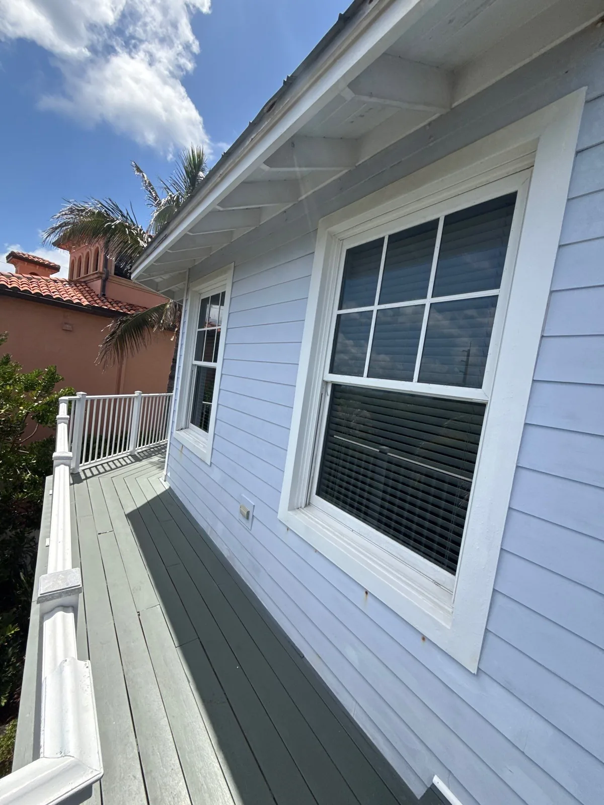 Exterior Painting in Juno Beach, Florida. Side deck with white lap siding, white window trim and grey painted decking under blue sky.