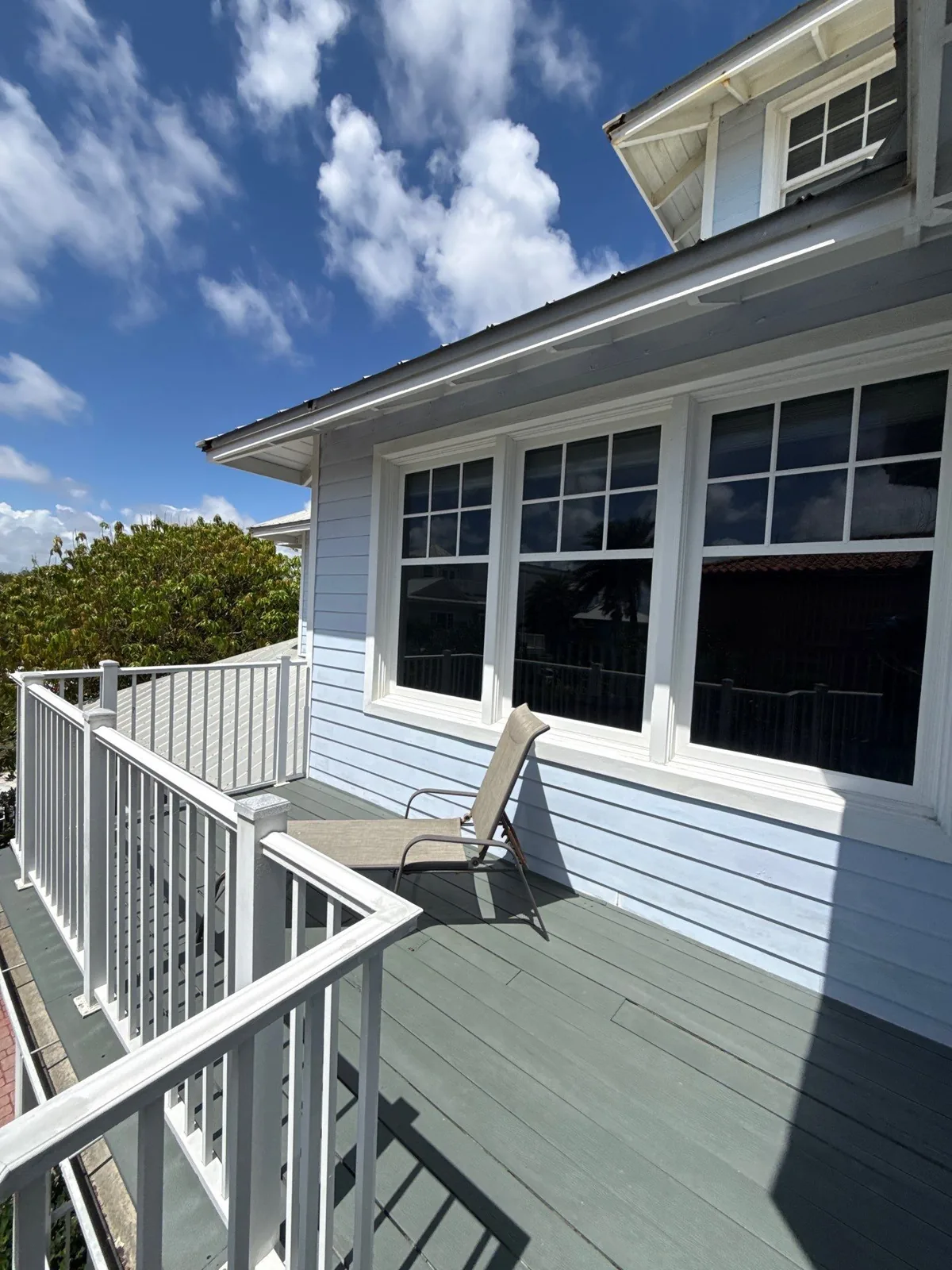 Exterior Painting in Juno Beach, Florida. Light blue lap-siding home exterior with white window trim, white deck railing and grey painted deck boards under blue sky.