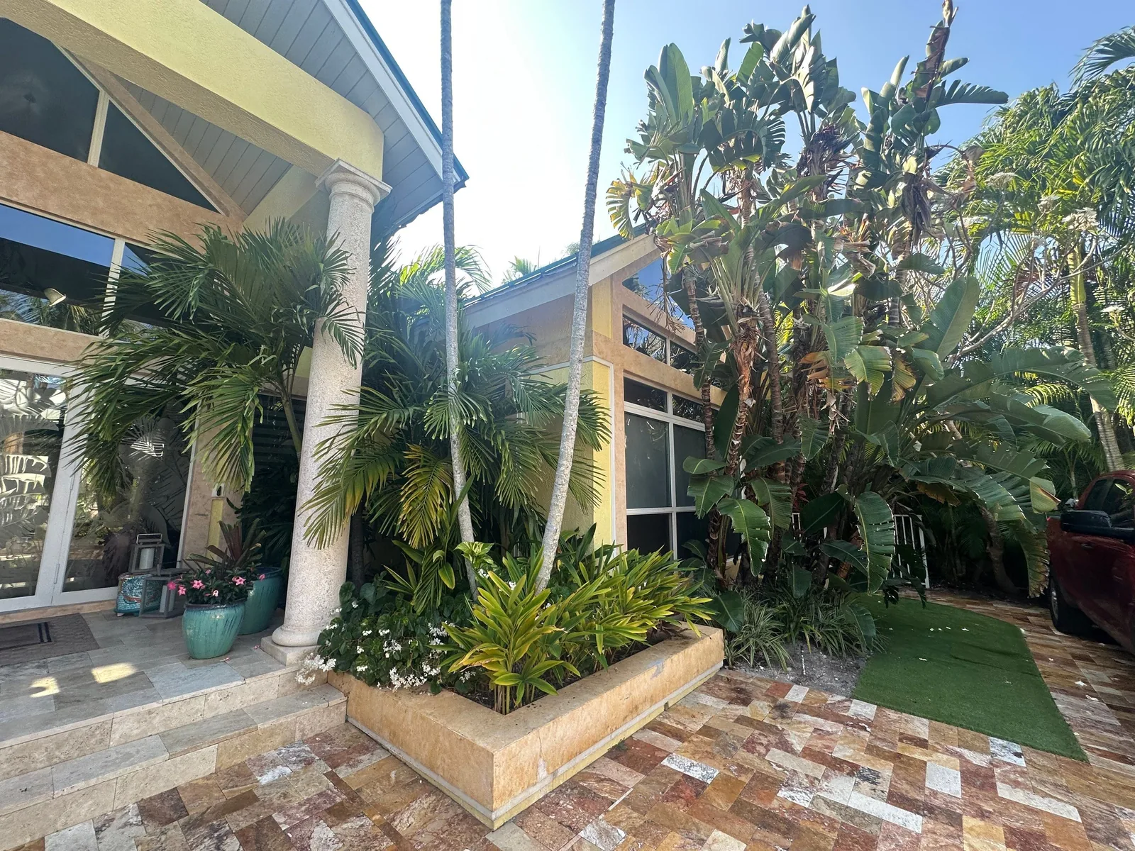 Exterior Painting in Juno Isles, Florida. Yellow stucco home exterior with white columns and trim, tall palms and a paver walkway.