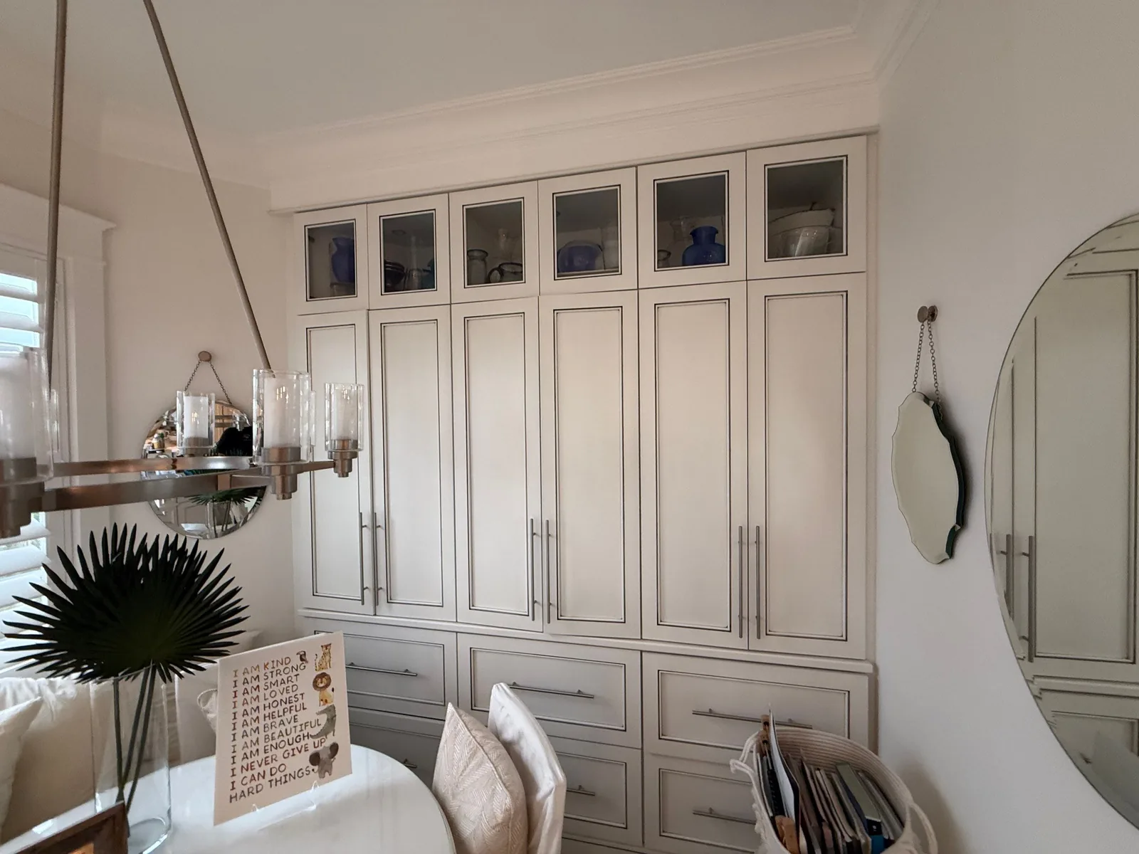 Cabinet Refinishing in Jupiter, Florida. Floor-to-ceiling white cabinetry with glass-front upper doors and chrome bar pulls, beside a round mirror.