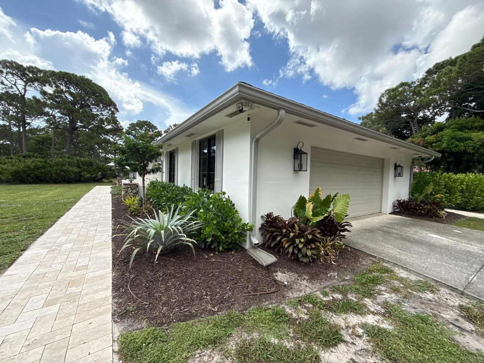 Exterior Painting in Jupiter, Florida. Single-storey white stucco house with attached garage, dark trim and landscaped beds under blue sky.