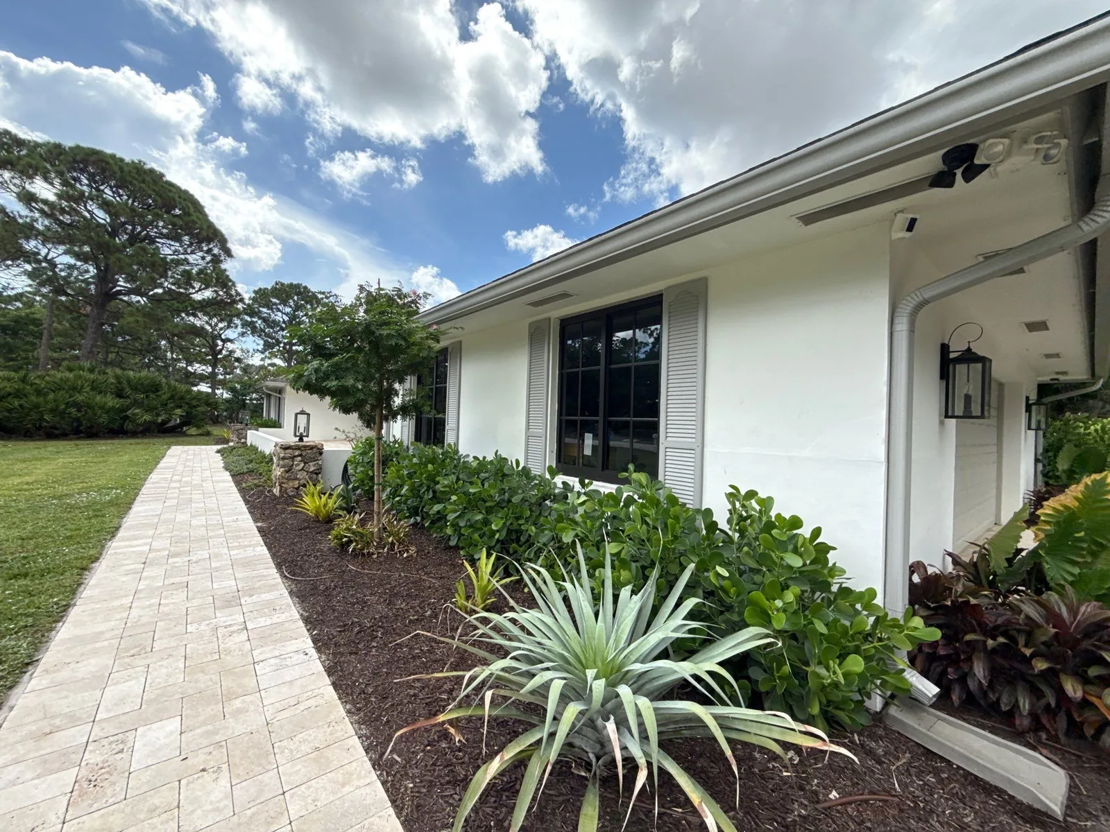 Exterior Painting in Jupiter, Florida. White stucco single-storey home with white shutters and paver walkway, viewed along the front elevation.