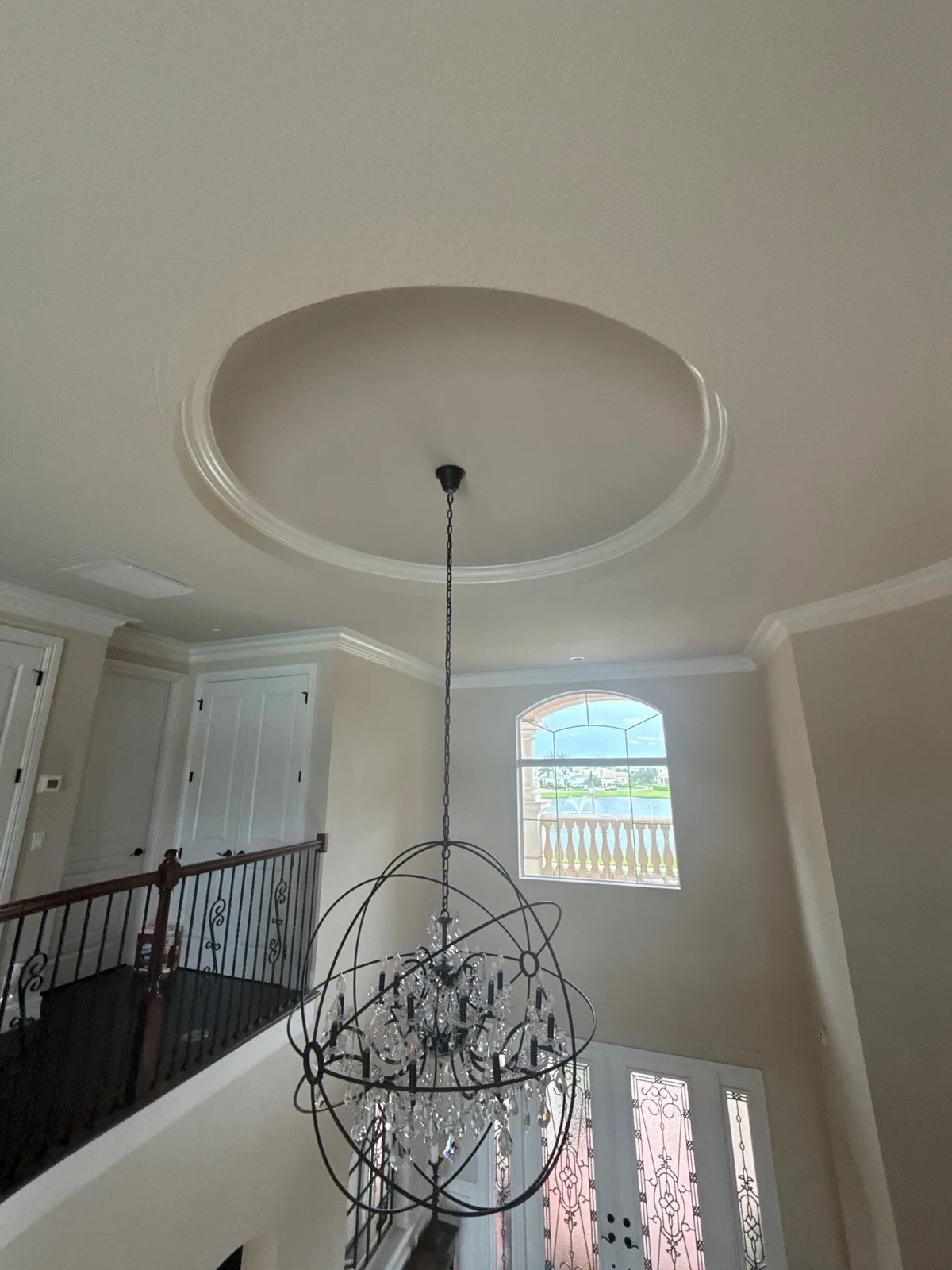 Interior Painting in Jupiter, Florida. Smooth painted ceiling with an oval recessed dome and crown moulding, orb chandelier hanging below in a two-storey stair hall.