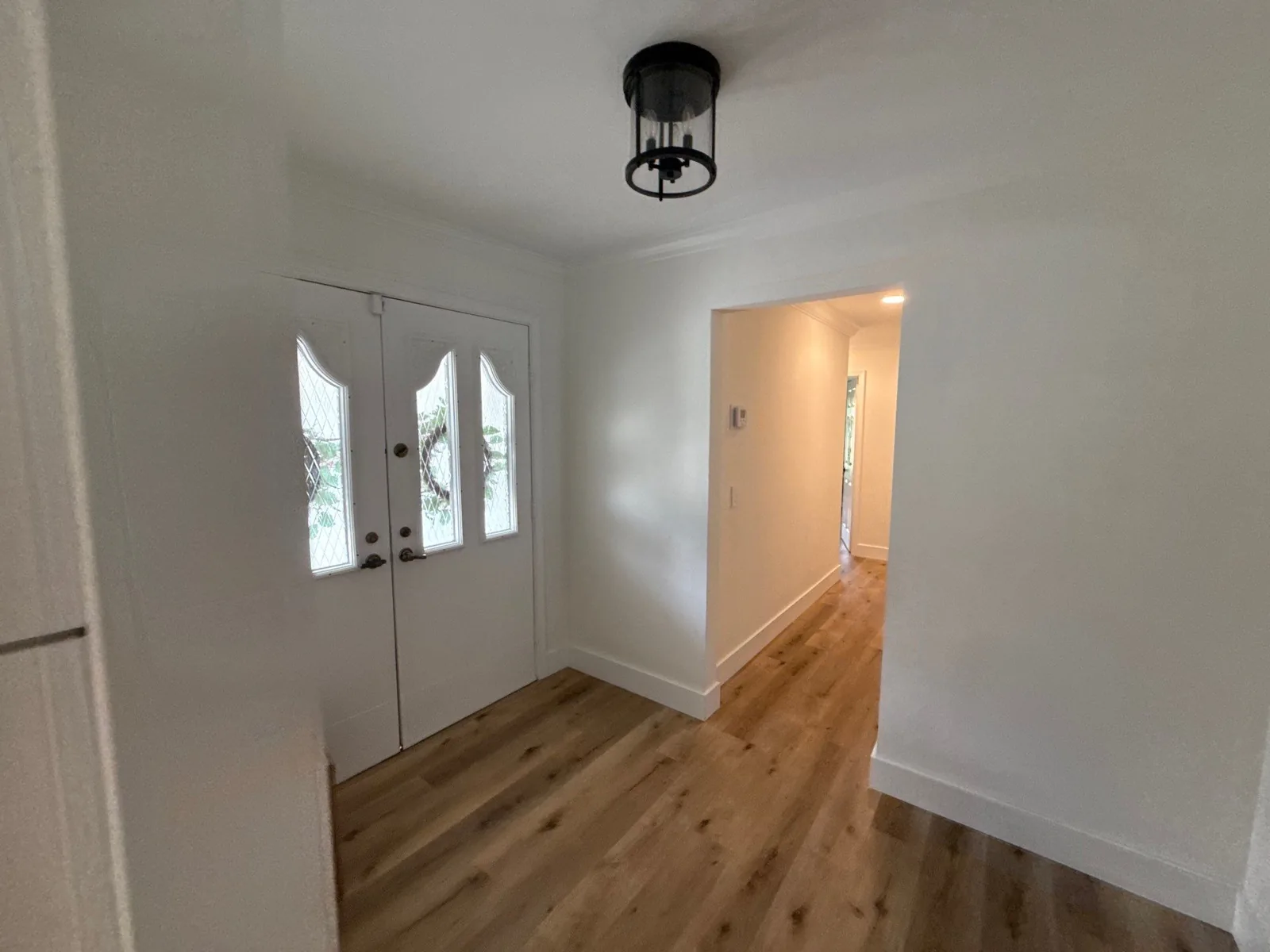 Interior Painting in Jupiter, Florida. Entryway with white double doors, white walls and trim, wood-look plank flooring and a black ceiling light.