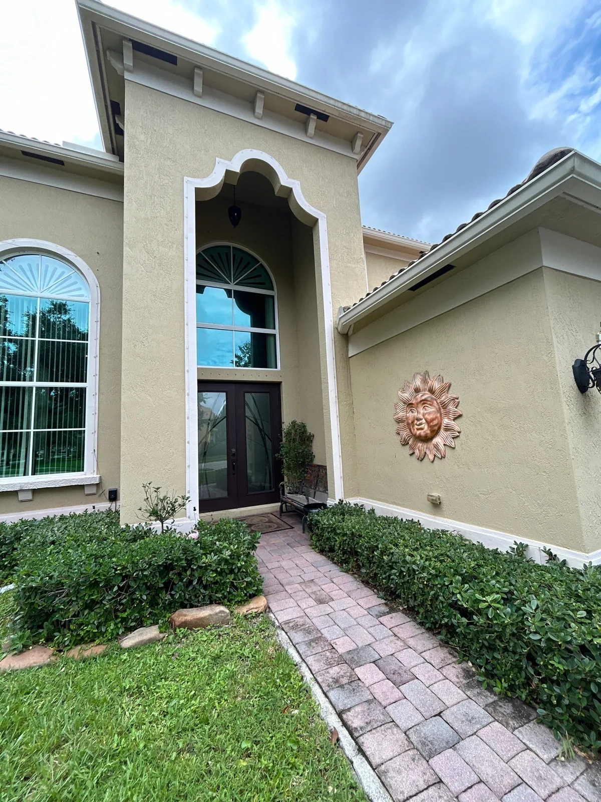 Exterior Painting in Lakewood Park, Florida. Painted stucco home entry with arched portico, glass double doors, decorative sun wall medallion and paver walkway.