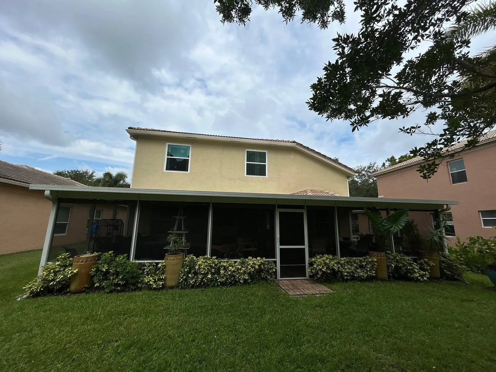 Exterior Painting in Lakewood Park, Florida. Rear elevation of a two-storey stucco home, pale yellow upper wall with white window trim above a screened porch and lawn.