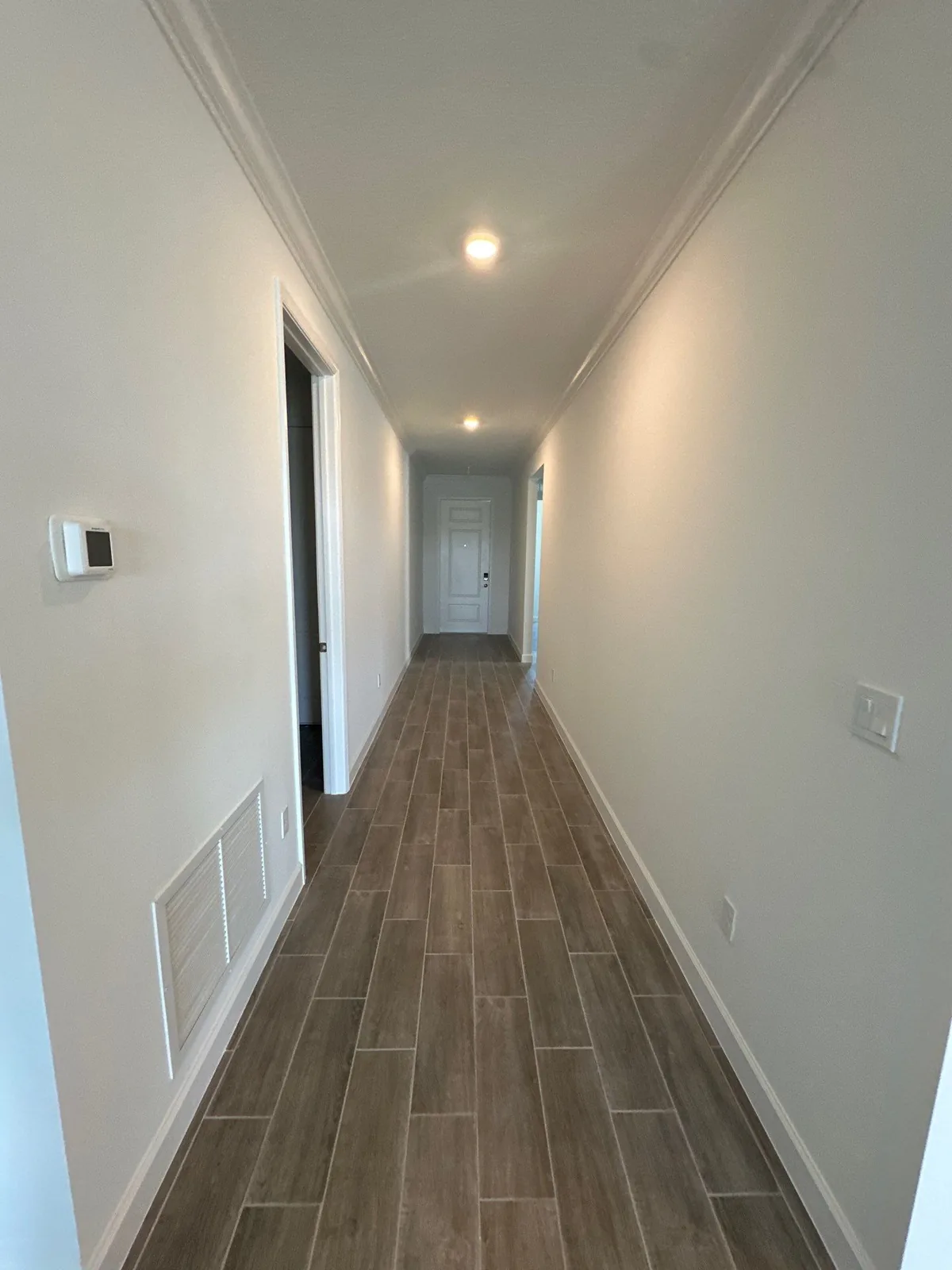 Interior Painting in Lakewood Park, Florida. Empty interior hallway with white painted walls and crown molding, wood-look tile floor, doorway at far end.