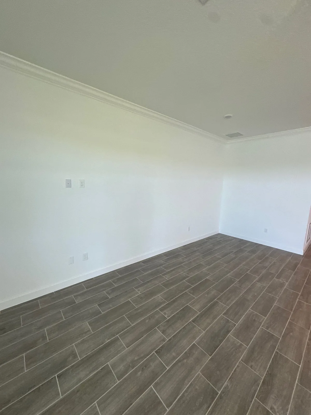 Interior Painting in Lakewood Park, Florida. Empty room corner with white painted walls, white crown molding and white ceiling, grey wood-look tile floor.