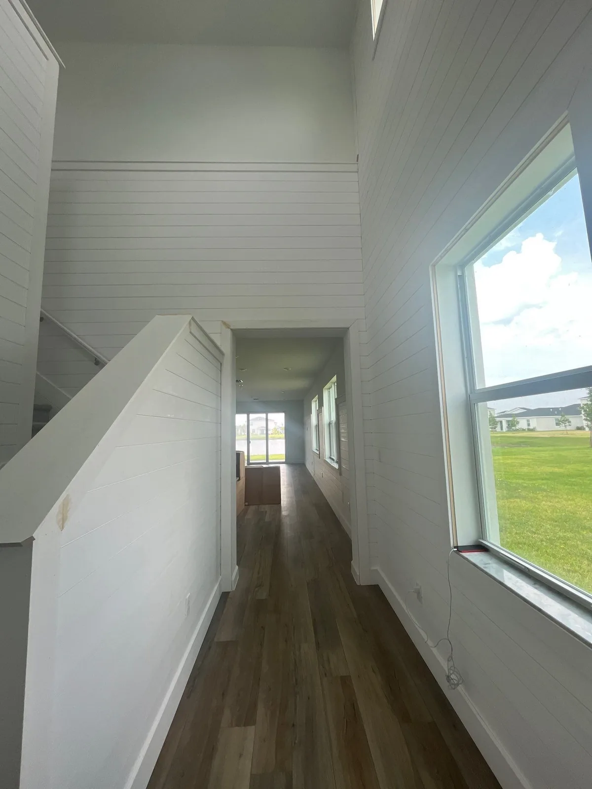 Interior Painting in Lakewood Park, Florida. Upstairs hallway with white painted shiplap walls, a large window and wood-look flooring.
