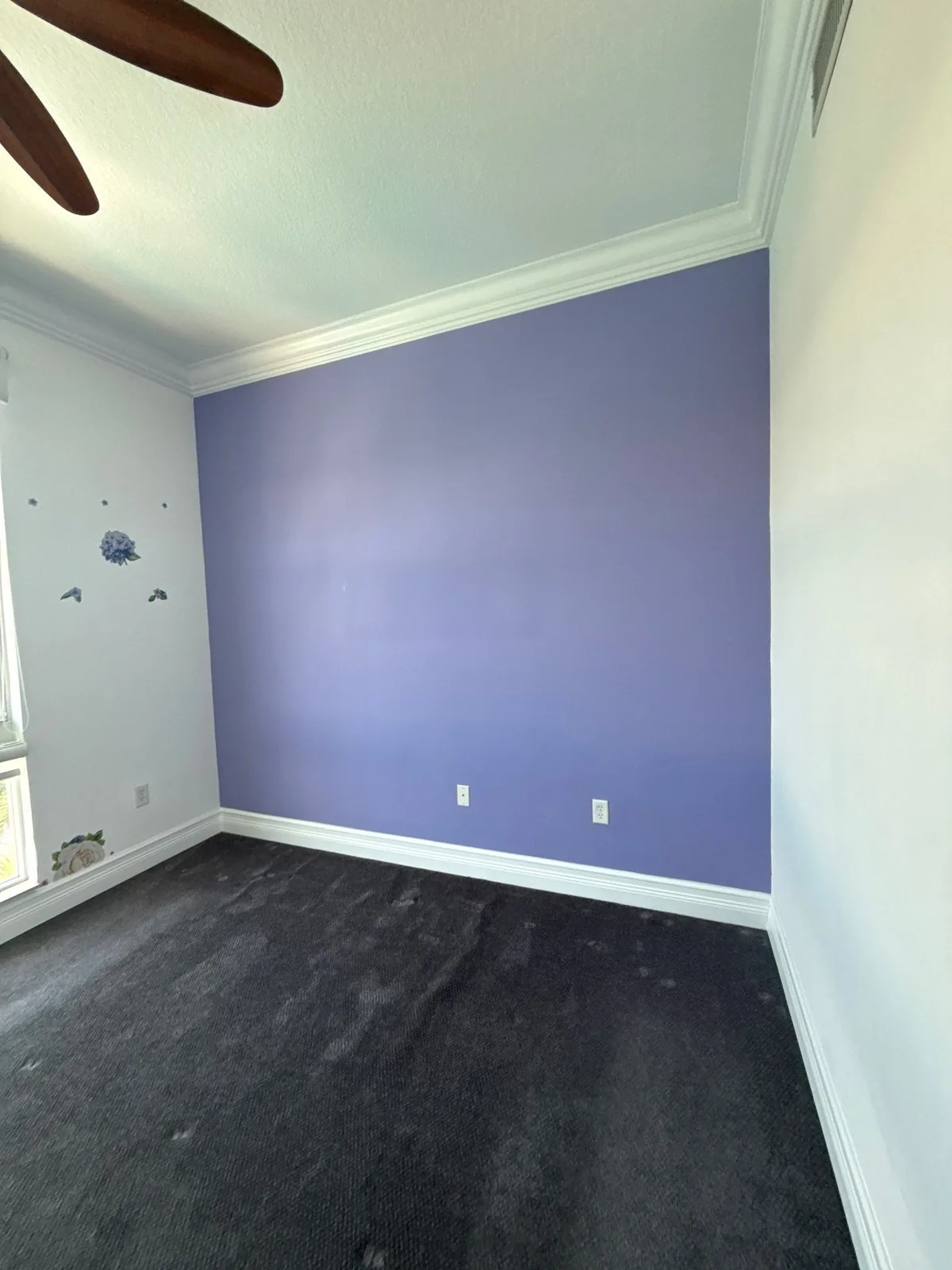 Interior Painting in Lantana, Florida. Bedroom with a purple accent wall, white crown molding and baseboards and dark grey carpet.