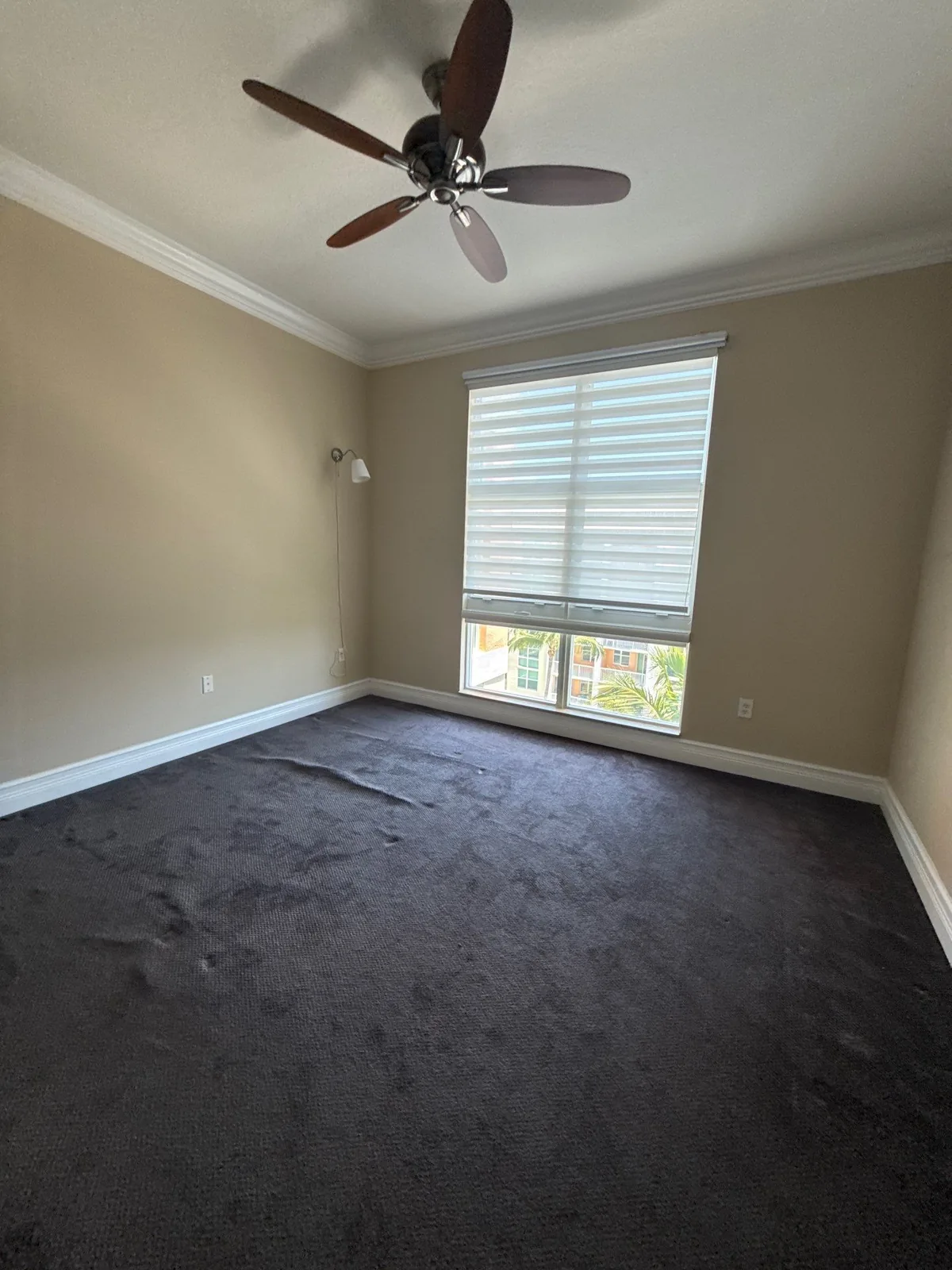 Interior Painting in Lantana, Florida. Empty bedroom with tan painted walls, white crown molding, a ceiling fan and a window with blinds.
