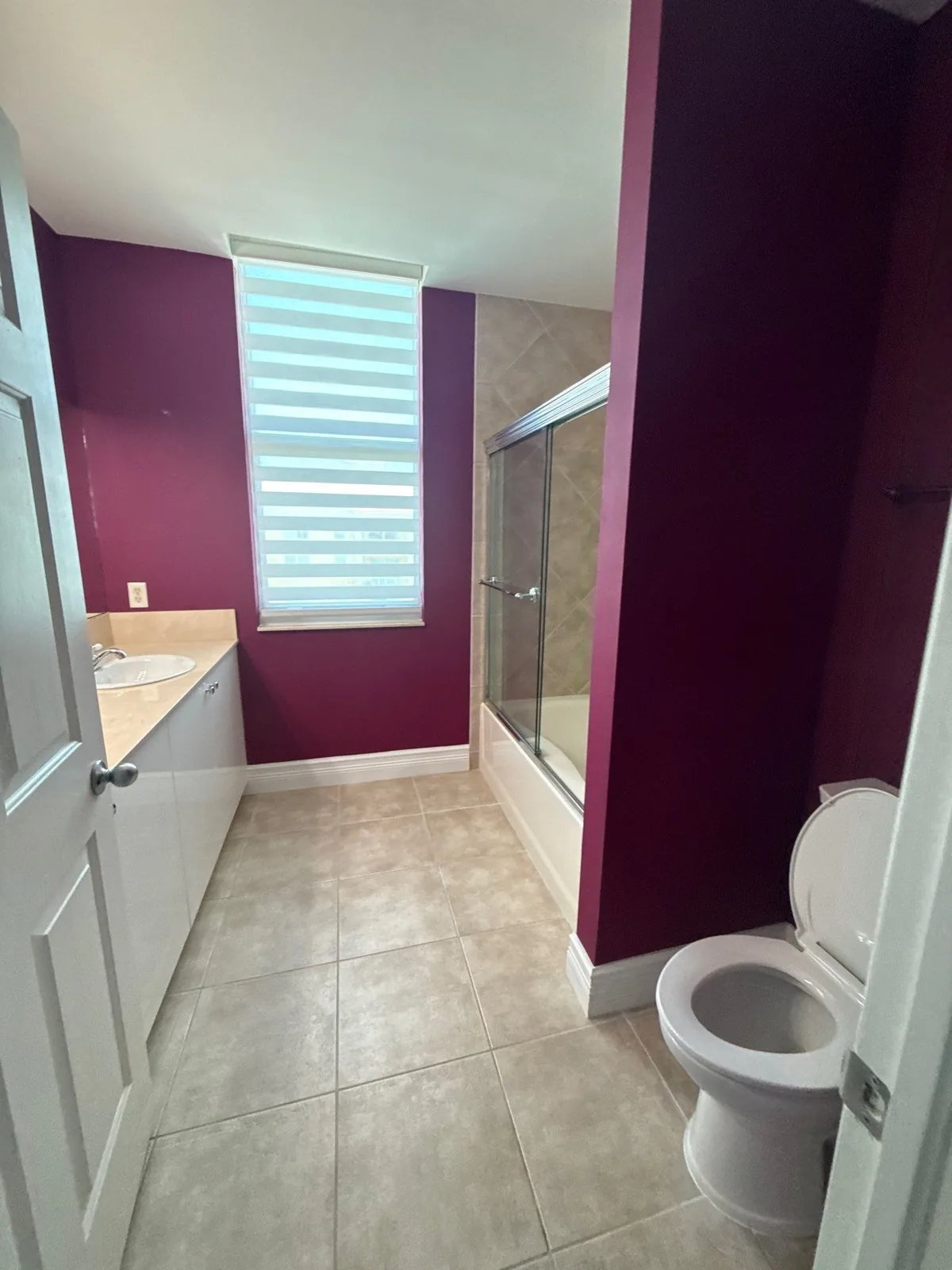 Interior Painting in Lantana, Florida. Bathroom with dark red painted walls, white trim, a tub and shower enclosure and tiled floor.