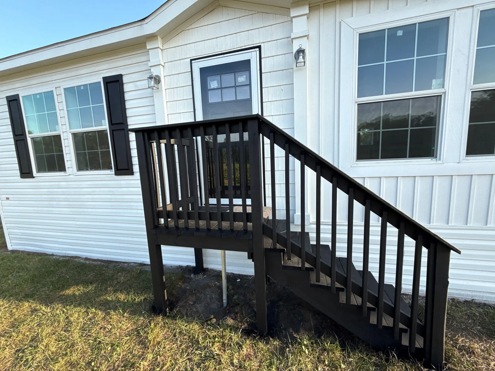 Exterior Painting in Melbourne, Florida. Single-storey home with white horizontal lap siding and black shutters, with dark-finished wood entry steps, deck and railing.
