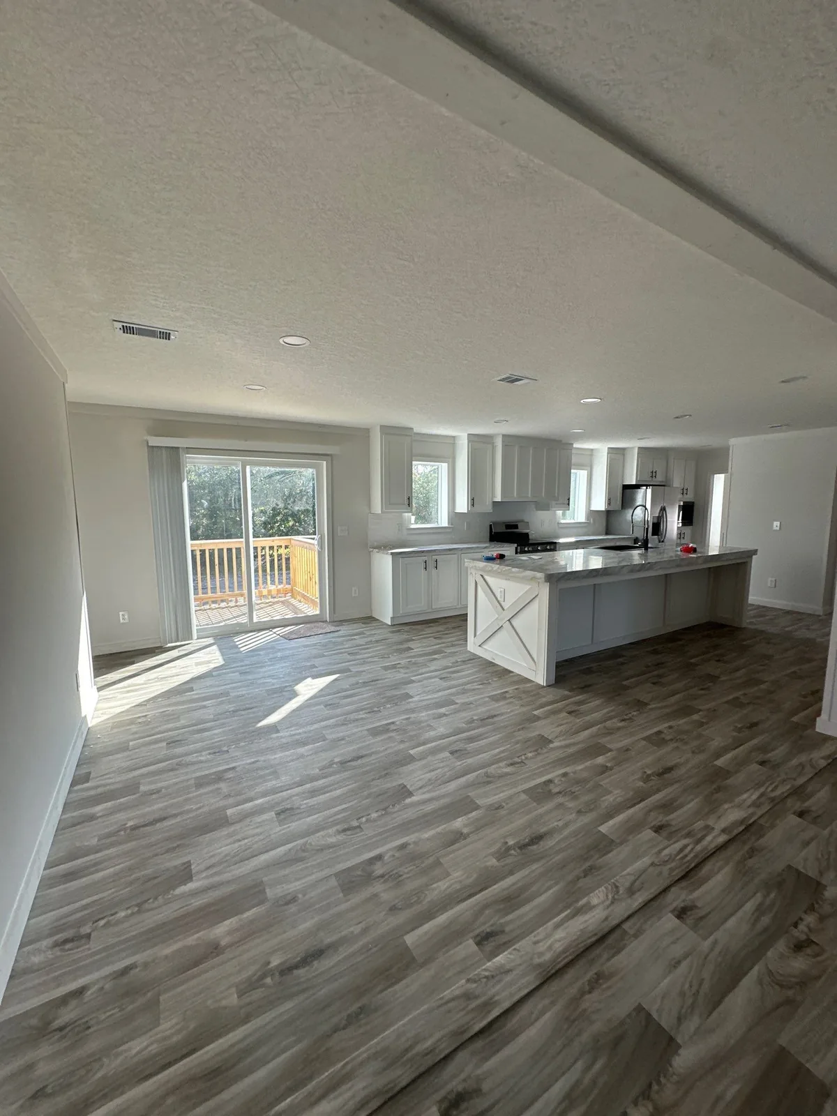 Interior Painting in Melbourne, Florida. Empty open-plan living and kitchen area with white walls, textured ceiling, white cabinets, an island and wood-look plank flooring.