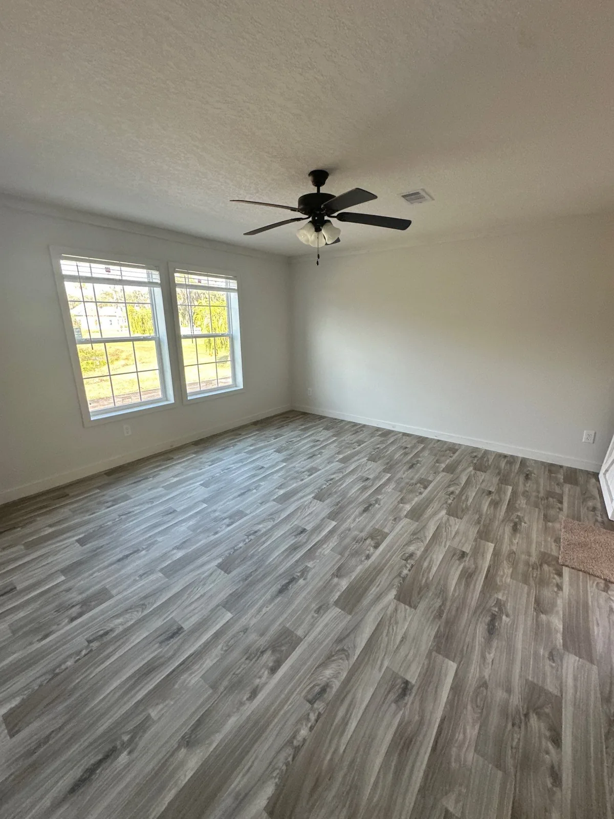 Interior Painting in Melbourne, Florida. Empty bedroom with white walls, two windows, crown moulding, ceiling fan and wood-look plank flooring.