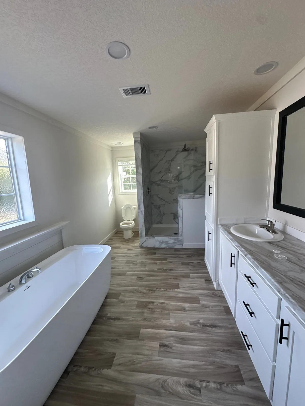 Interior Painting in Melbourne, Florida. Bathroom with white walls, freestanding tub, white shaker vanity cabinets, tiled walk-in shower and wood-look plank flooring.