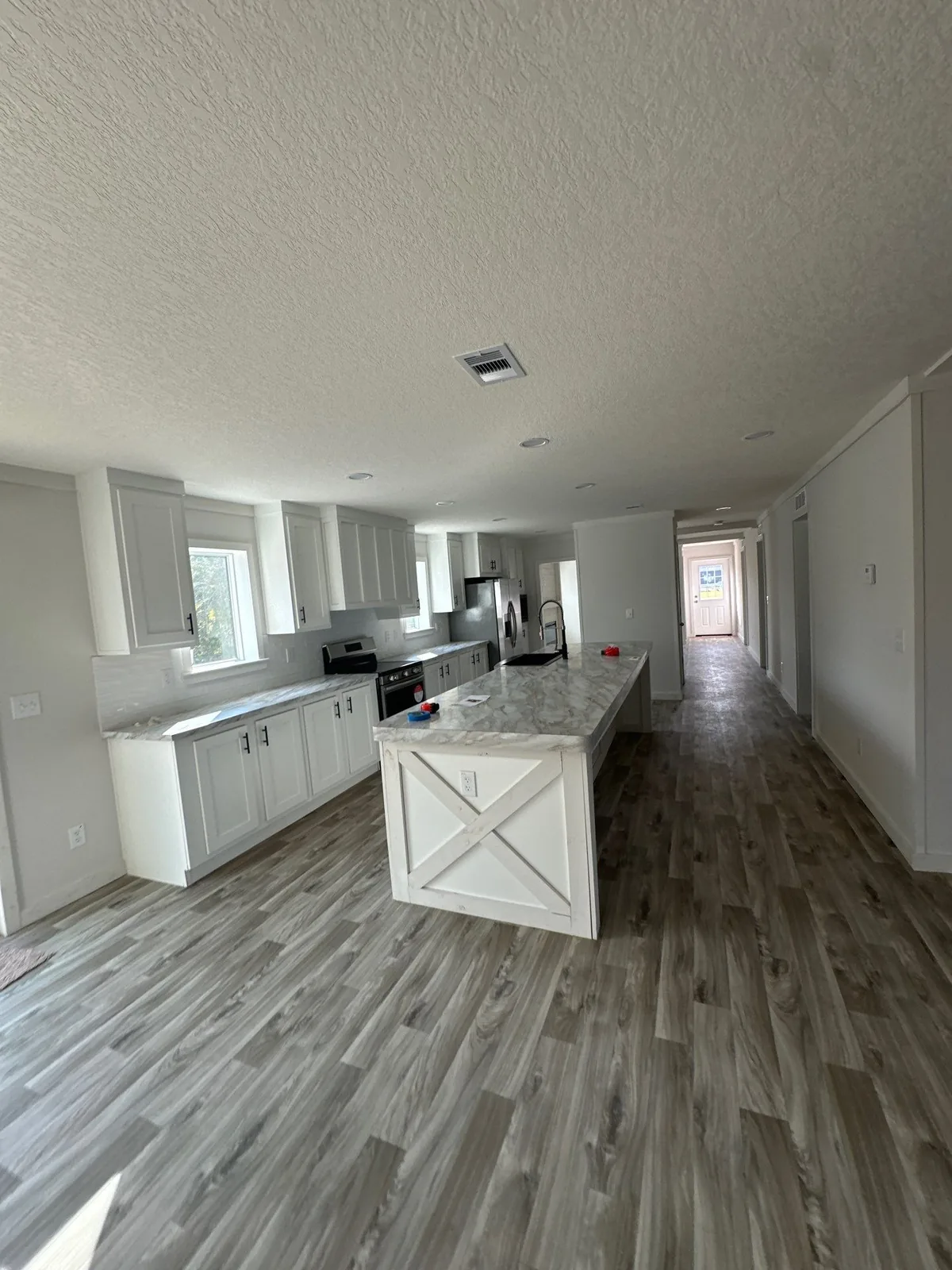 Interior Painting in Melbourne, Florida. Kitchen with white cabinets, stone countertops, a large island with X-panel detail and wood-look plank flooring.