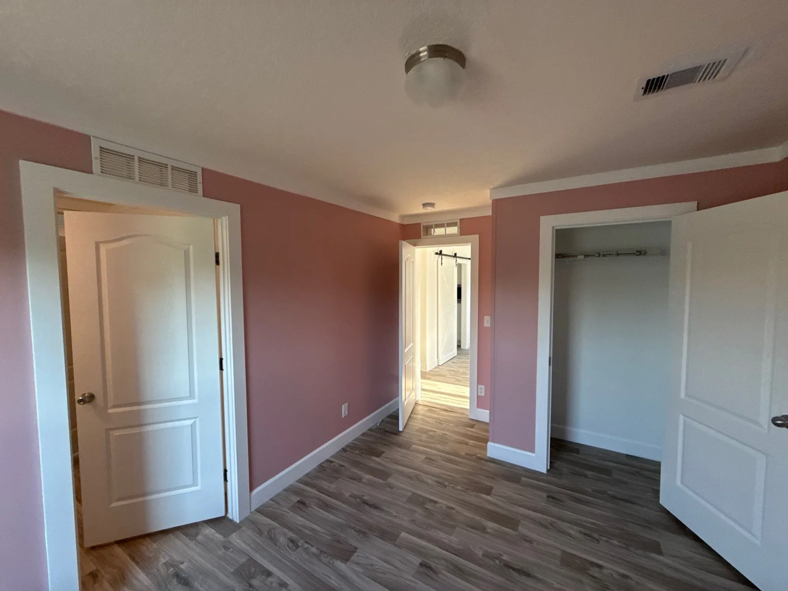 Interior Painting in Melbourne, Florida. Empty bedroom with dusty rose walls, white trim and panel doors, an open closet and grey wood-look flooring.