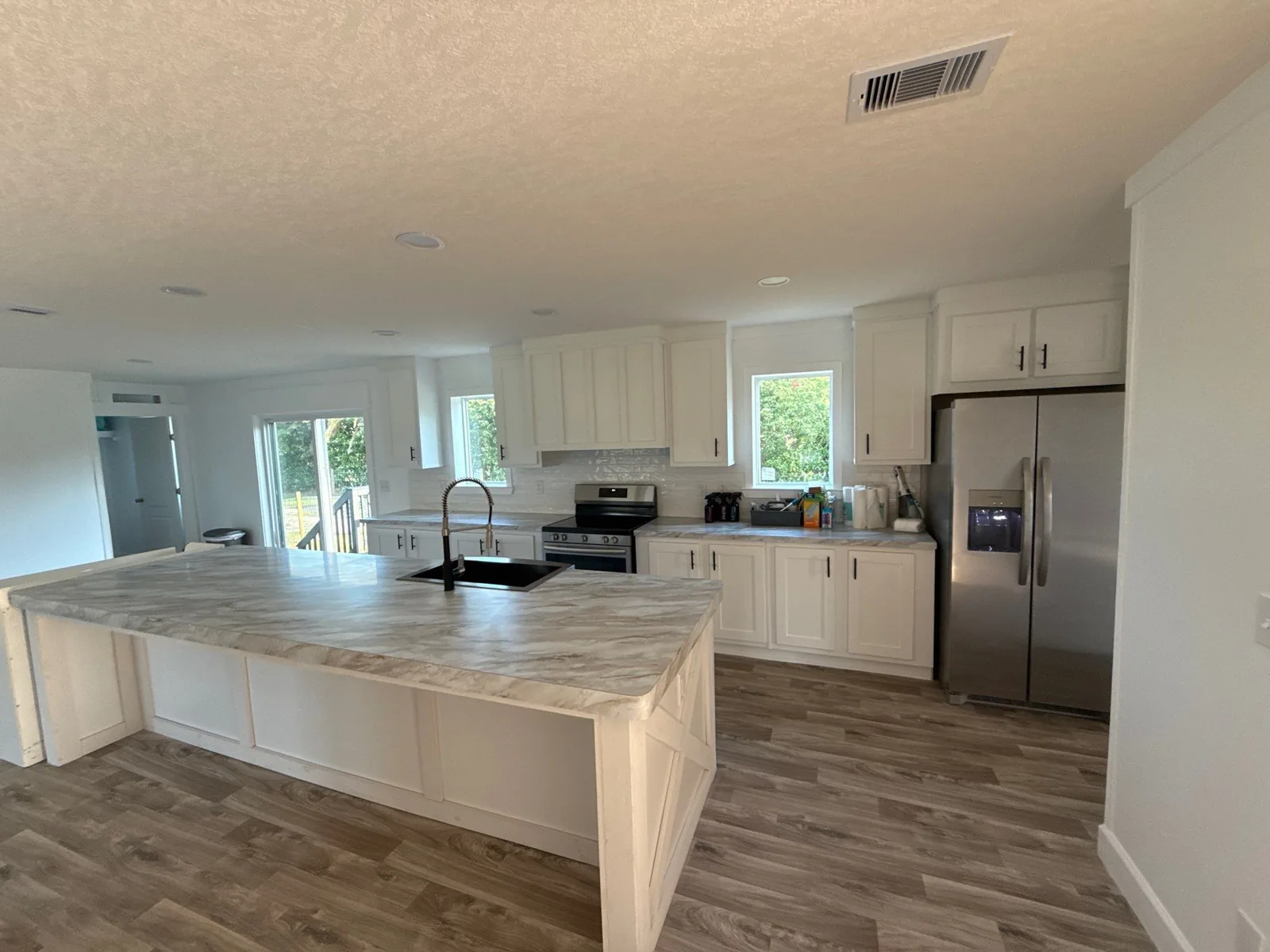 Interior Painting in Melbourne, Florida. Open kitchen with white shaker cabinets, large island with stone-look countertop, stainless steel appliances and white walls.