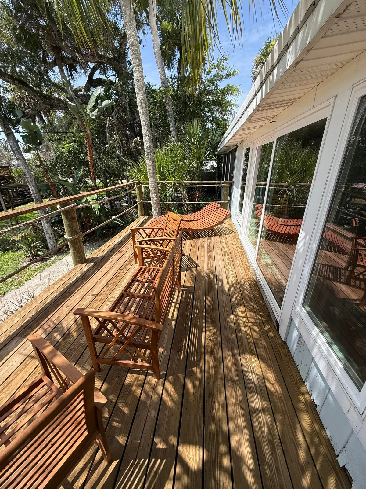 Exterior Painting in Micco, Florida. Wood deck with wooden chairs running alongside a house with white siding and large windows, palms behind.