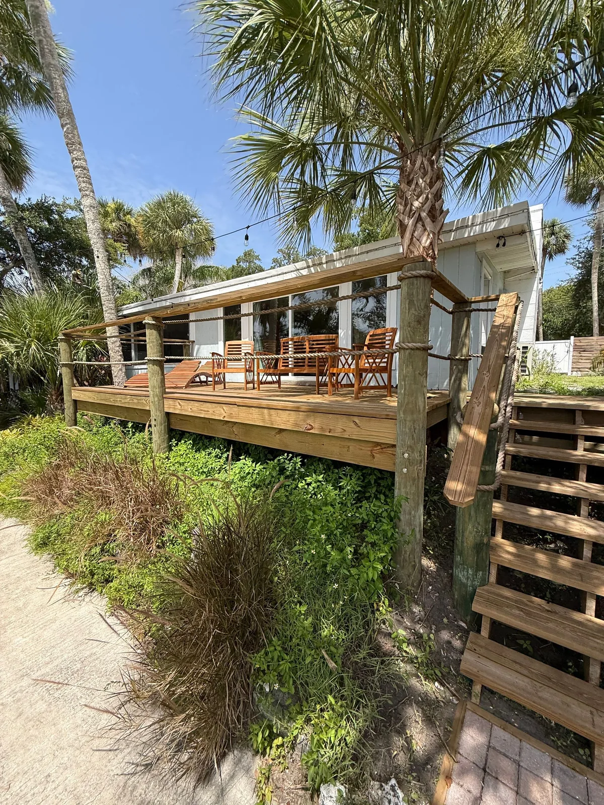 Exterior Painting in Micco, Florida. Single-storey house with a raised wood deck and railing, framed by palm trees under a clear sky.