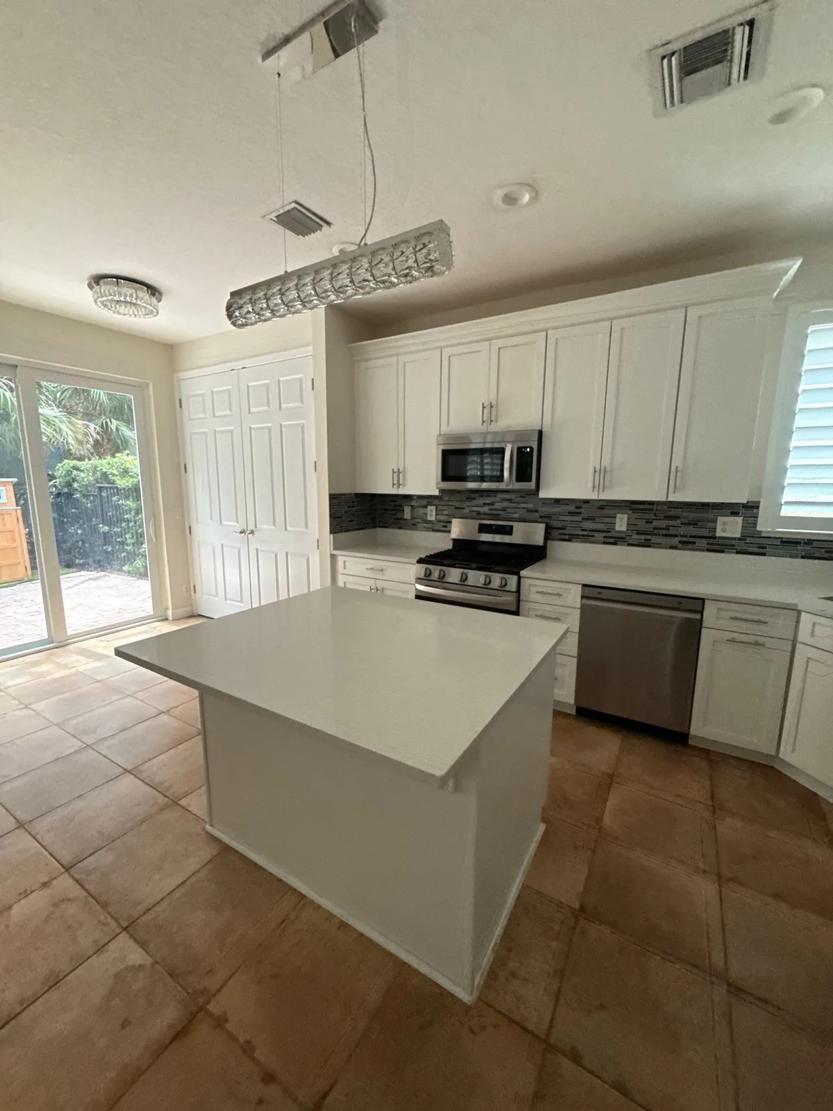 Cabinet Refinishing in North Palm Beach, Florida. Kitchen with white cabinets, dark tile backsplash, stainless steel appliances and a white island.