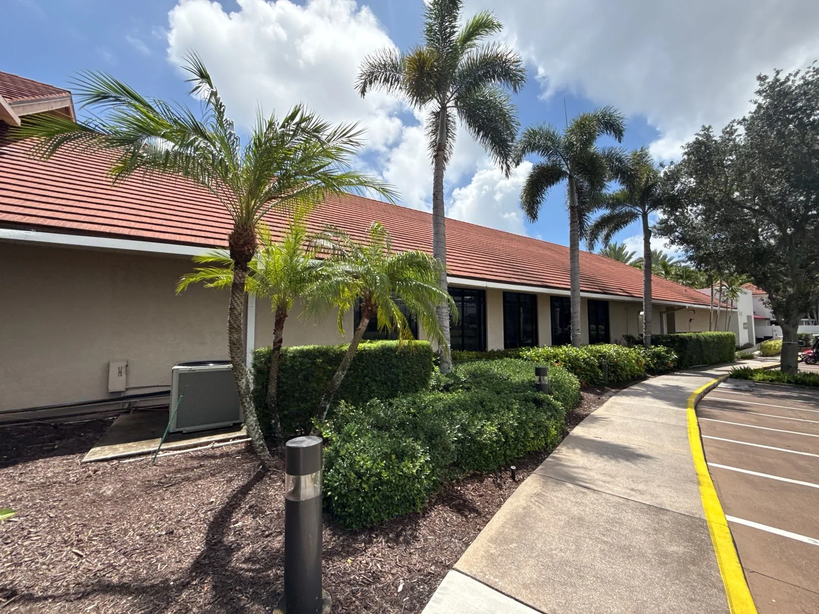 Commercial Painting in North Palm Beach, Florida. Single-storey commercial plaza with beige stucco, red tile roof and dark storefronts, palms and hedges along the sidewalk.