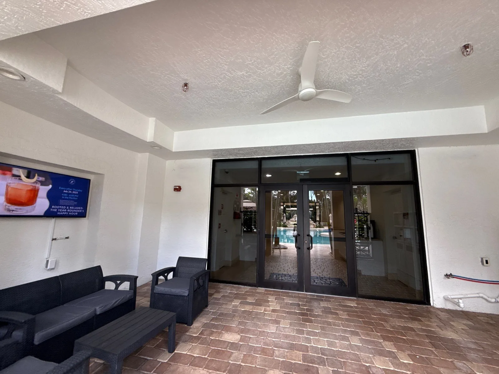Commercial Painting in North Palm Beach, Florida. Covered building entry with white painted ceiling and walls, ceiling fan, dark glass double doors and outdoor seating.