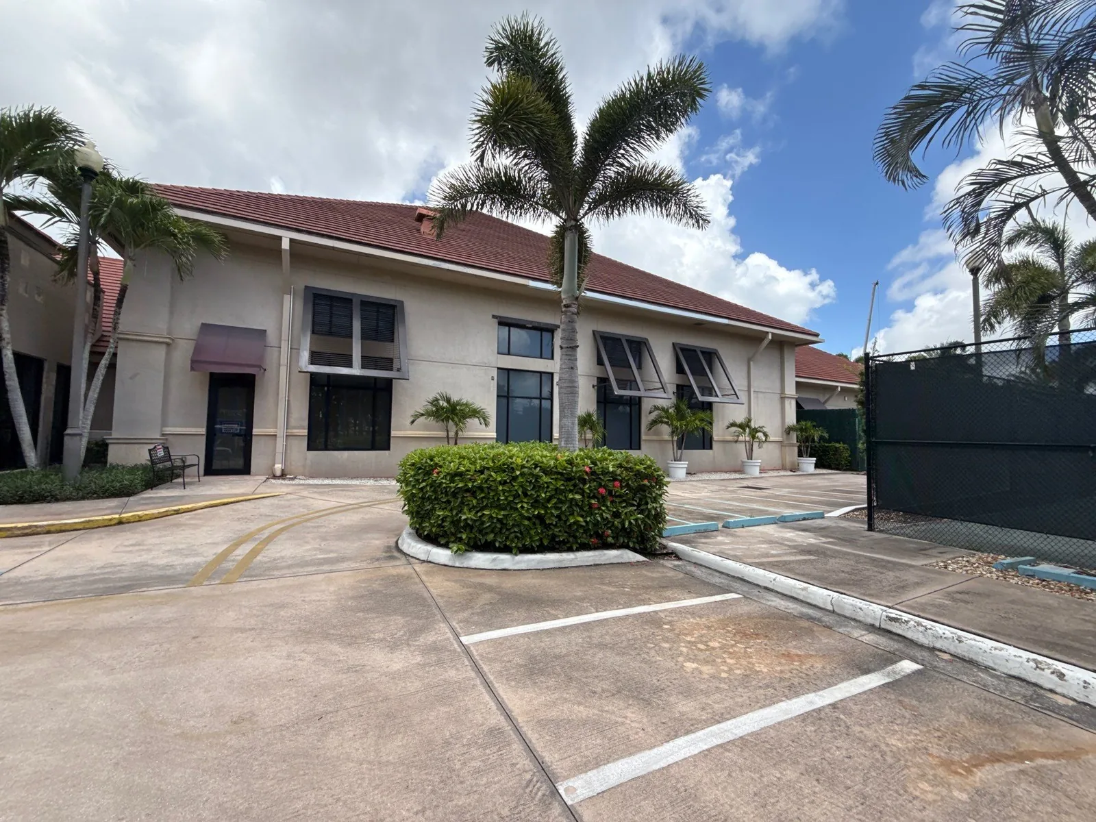 Commercial Painting in North Palm Beach, Florida. Two-storey beige stucco commercial building with red tile roof, dark window awnings and palms, viewed from the parking lot.