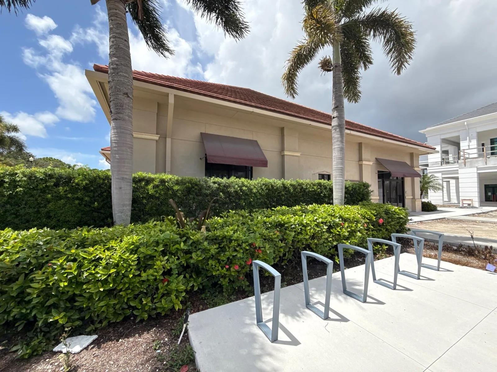 Commercial Painting in North Palm Beach, Florida. Tan single-storey commercial building with tile roof and dark awnings, hedges and bike racks in the foreground.