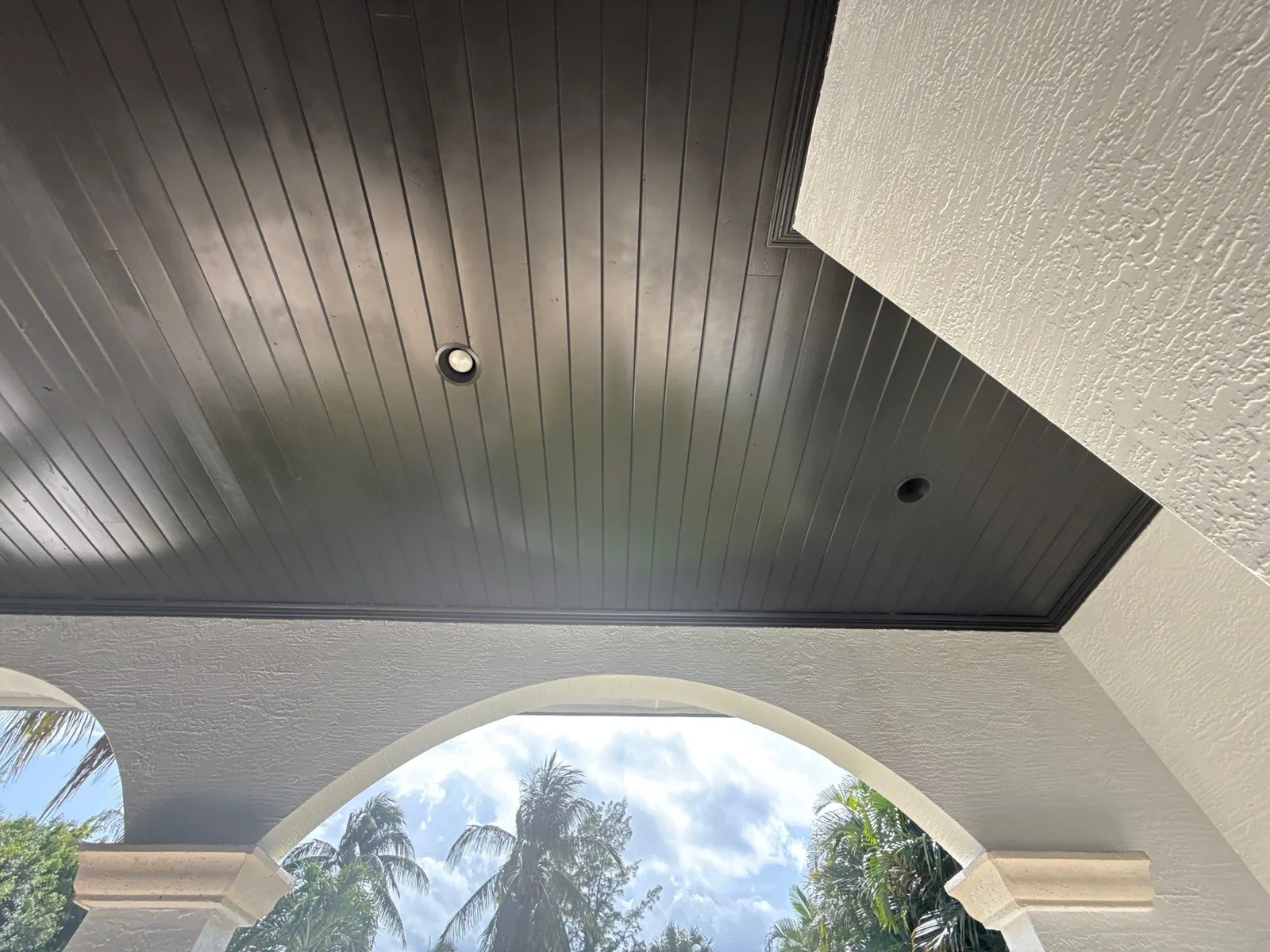 Exterior Painting in North Palm Beach, Florida. Dark-painted tongue-and-groove covered porch ceiling with recessed lights, above white stucco arches.