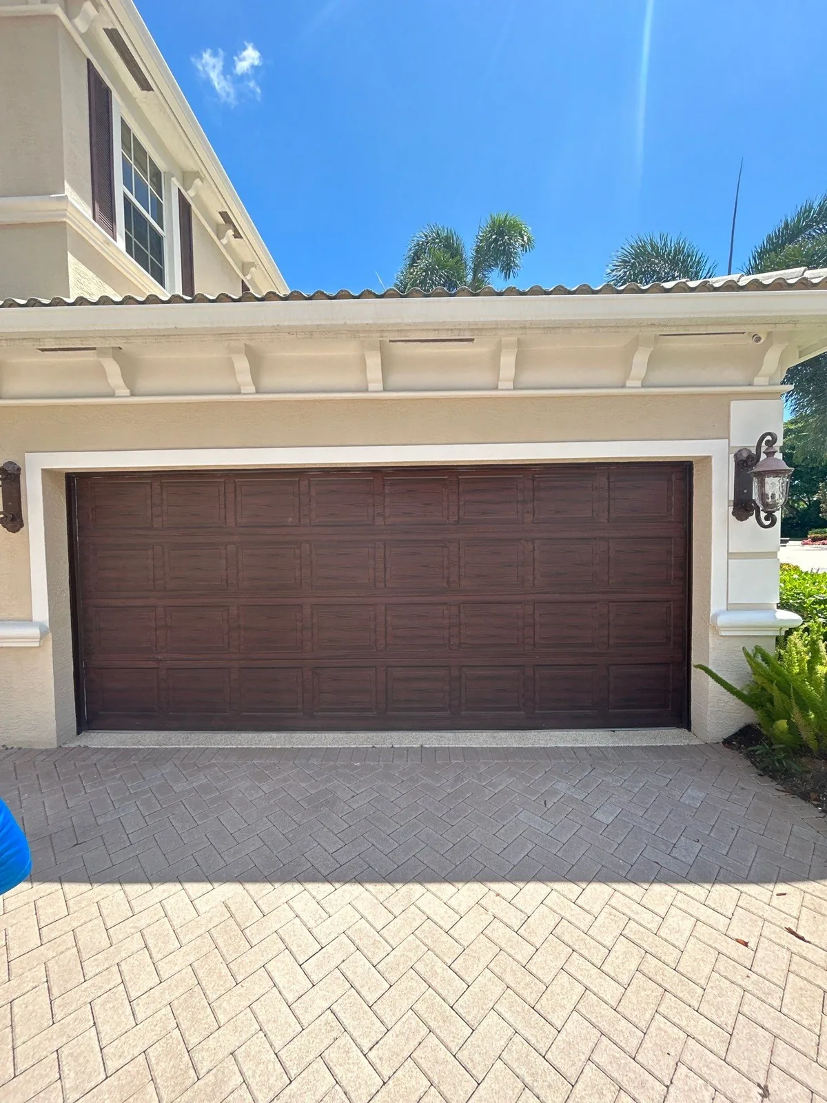 Exterior Painting in North Palm Beach, Florida. Two-car garage door with a dark wood-grain finish set in a cream stucco house above a paver driveway.