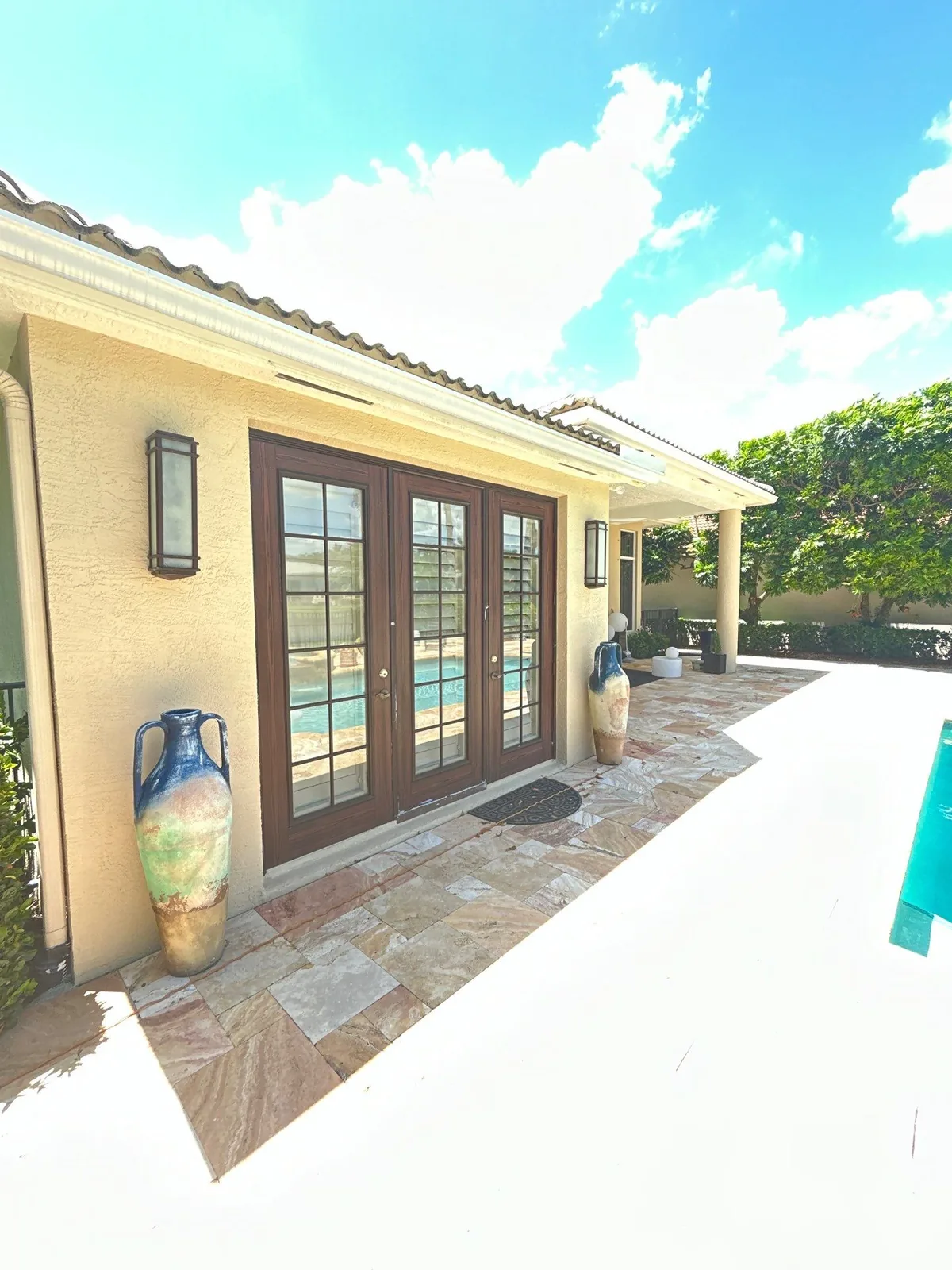 Exterior Painting in North Palm Beach, Florida. Covered pool patio with cream stucco walls, dark wood-grain french doors and decorative urns on stone paving.