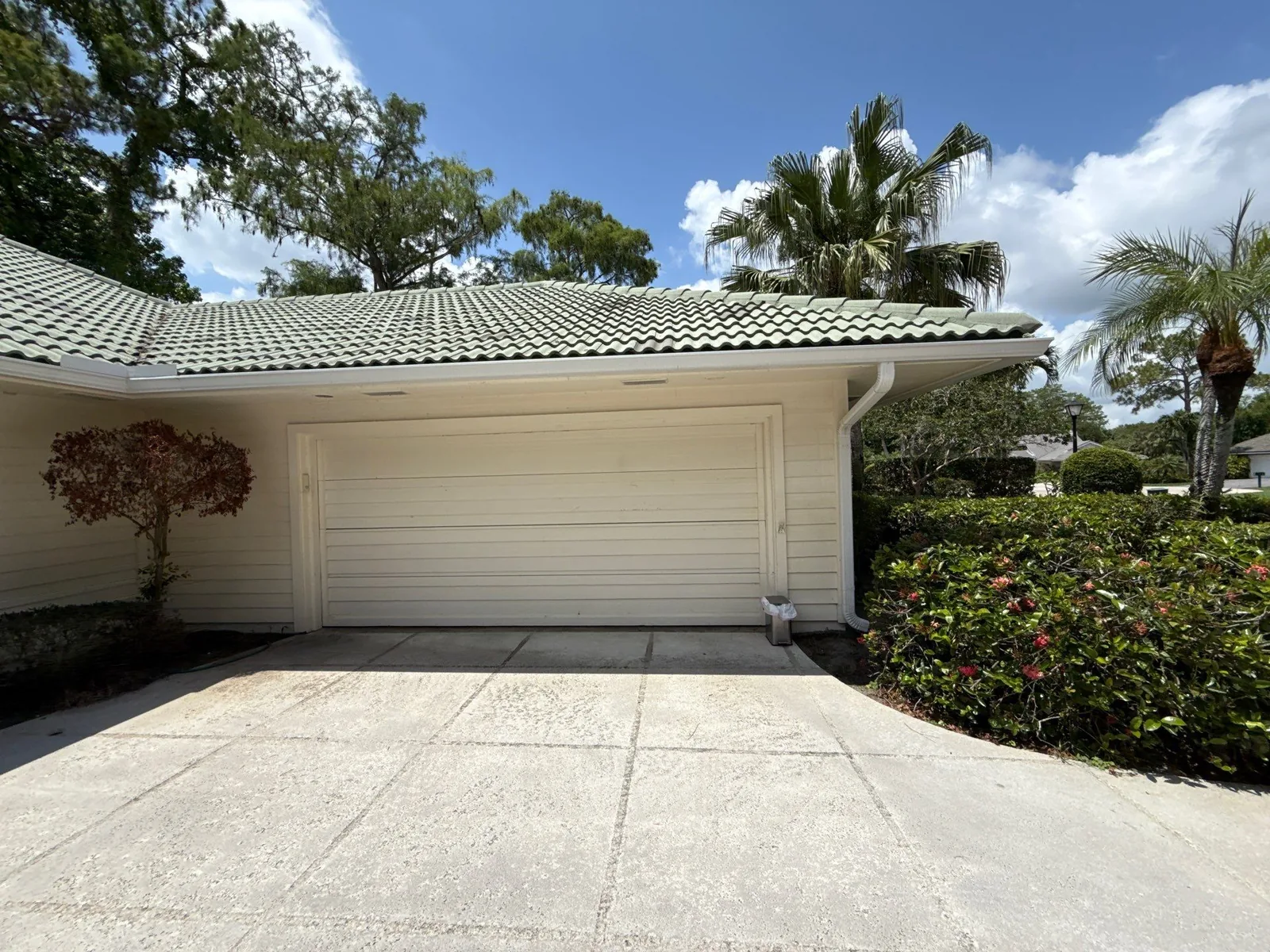 Exterior Painting in North Palm Beach, Florida. Single-storey home with cream horizontal siding, white garage door and green tile roof.