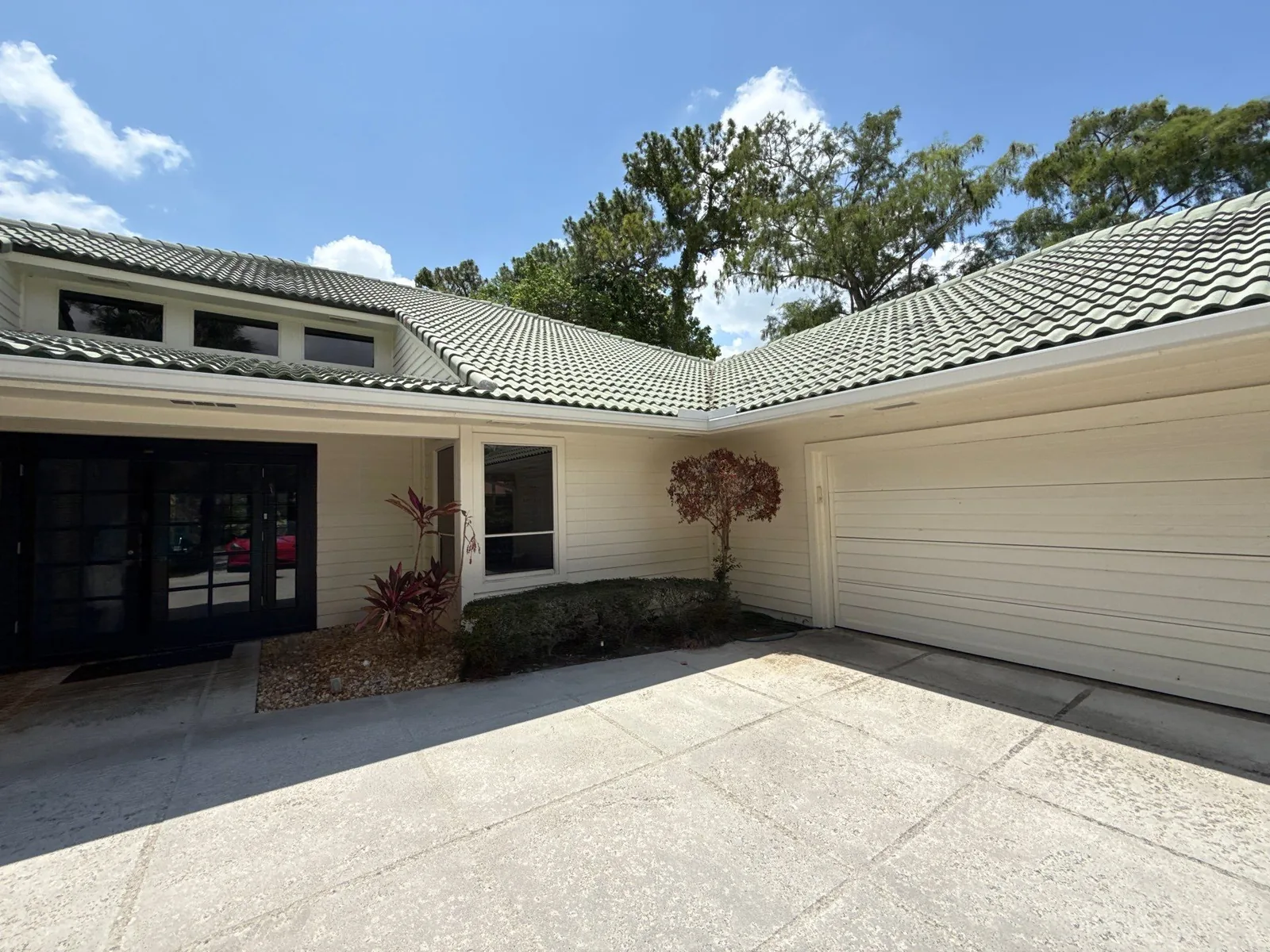 Exterior Painting in North Palm Beach, Florida. Front entry of a single-storey home with cream siding, dark glass doors and green tile roof.