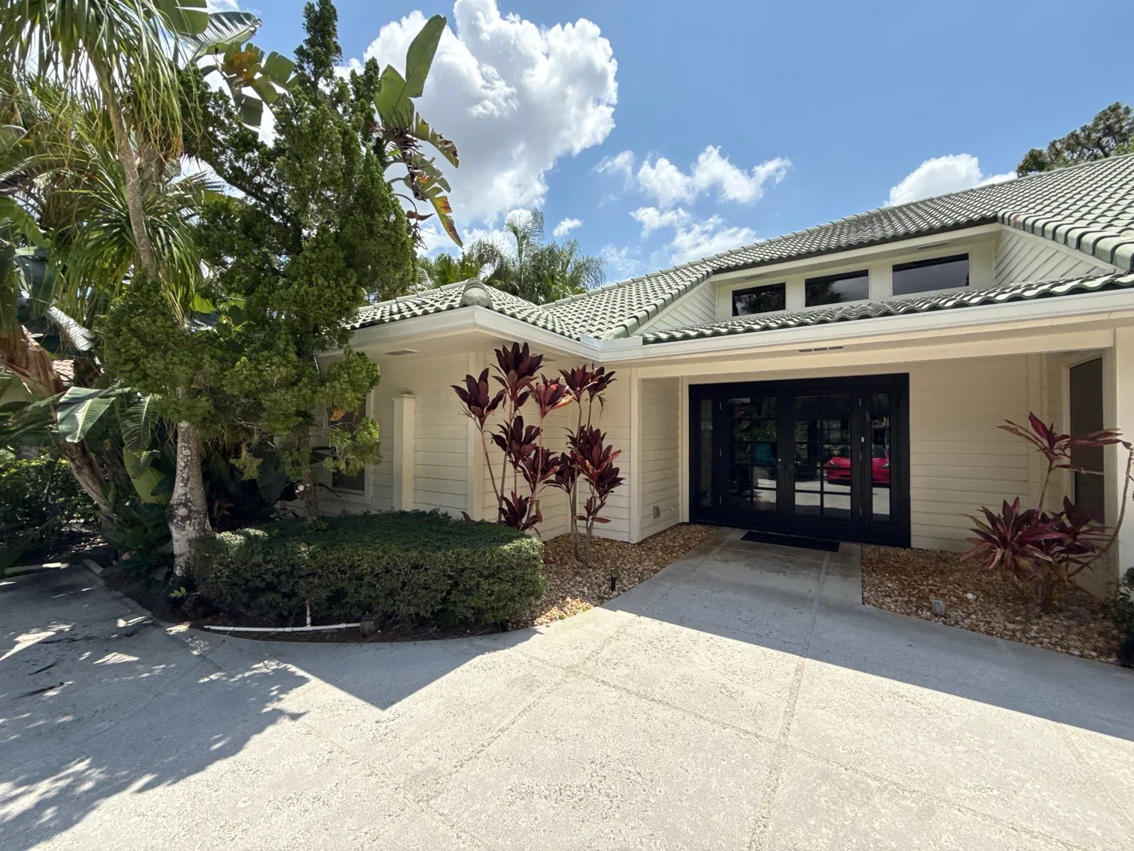 Exterior Painting in North Palm Beach, Florida. Covered front entrance of a home with cream siding and green tile roof, framed by tropical planting.
