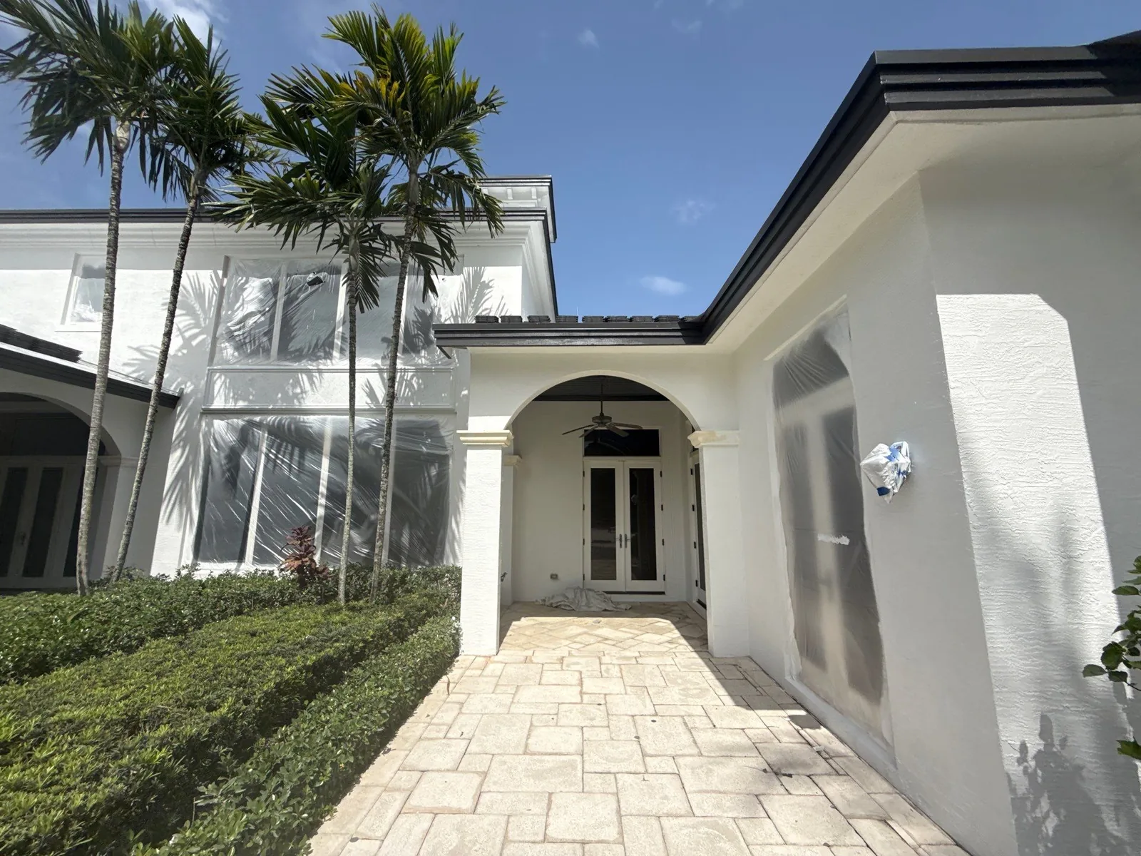 Exterior Painting in North Palm Beach, Florida. White stucco home entry with columned portico, dark fascia and paver walkway under blue sky.