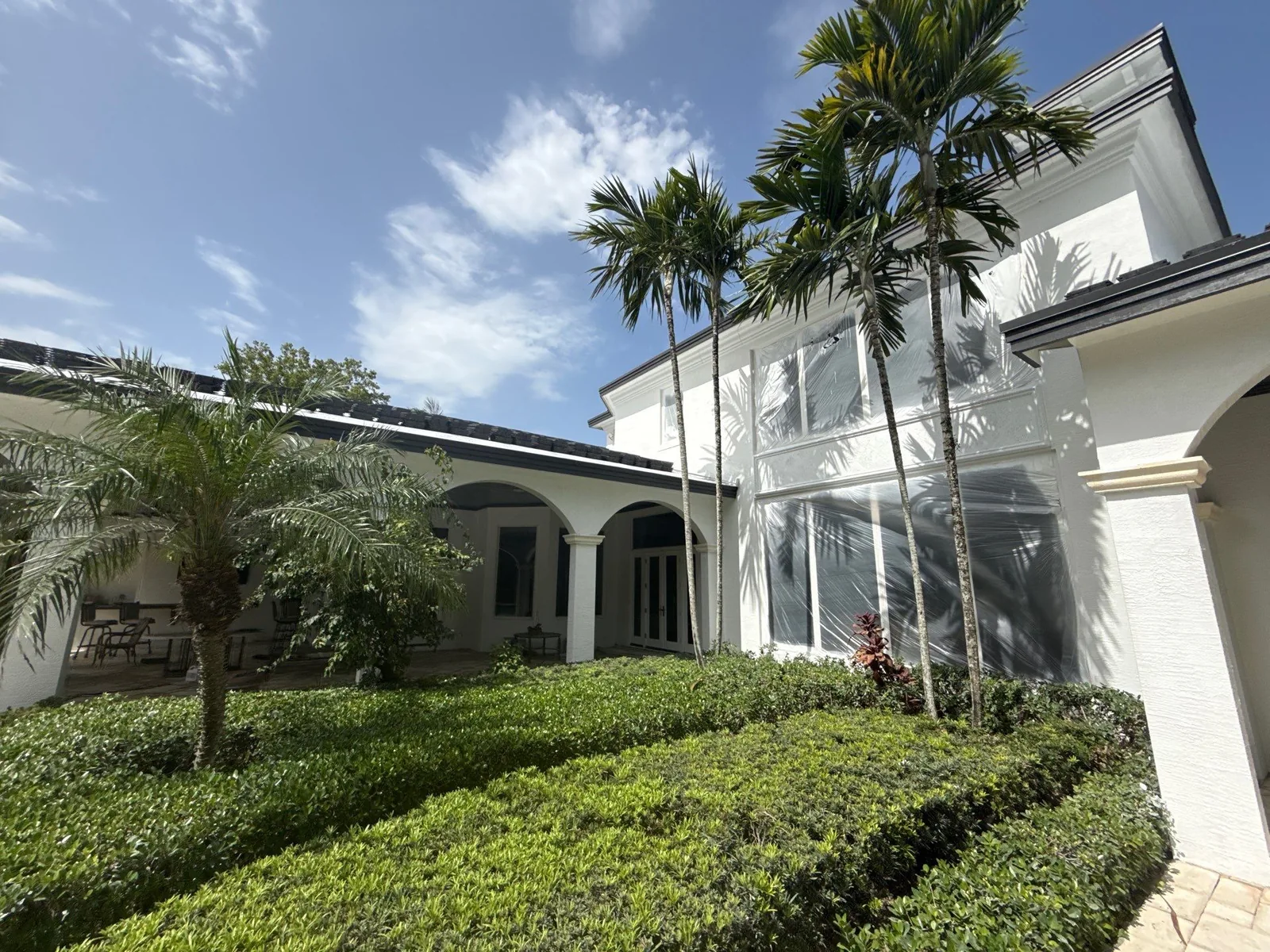 Exterior Painting in North Palm Beach, Florida. Two-storey white stucco home exterior with screened window openings, palms and clipped hedges in front.
