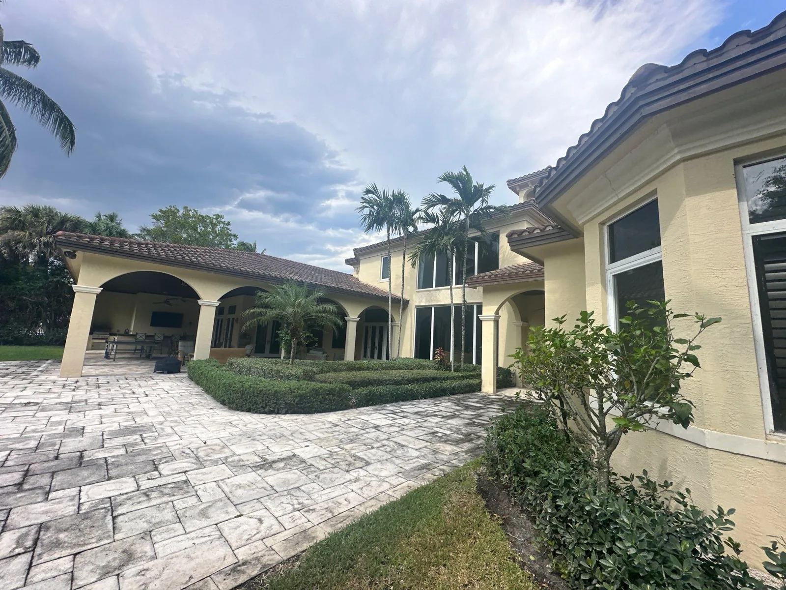 Exterior Painting in North Palm Beach, Florida. Large stucco home with arched covered loggia, barrel tile roof, paver drive and palms under a blue sky.