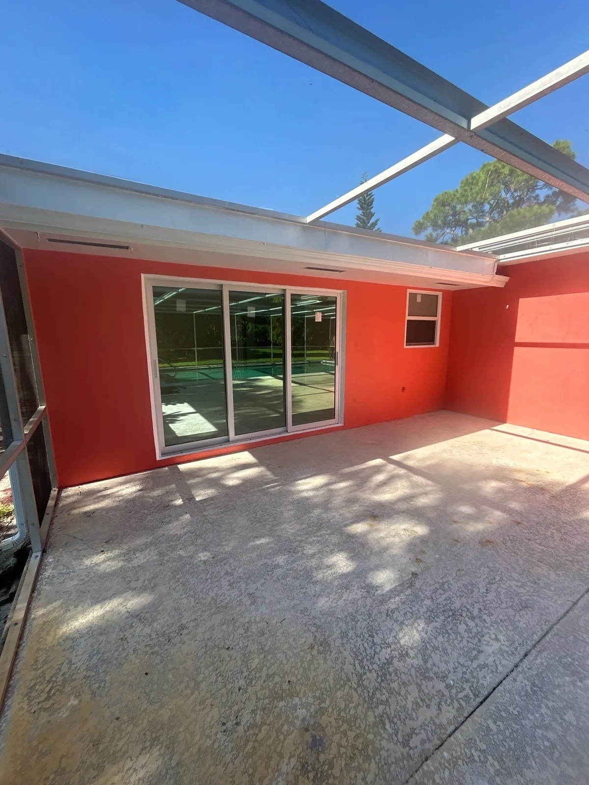 Exterior Painting in North River Shores, Florida. Screened patio with a coral painted stucco wall, white sliding glass door and white soffit over a concrete slab.
