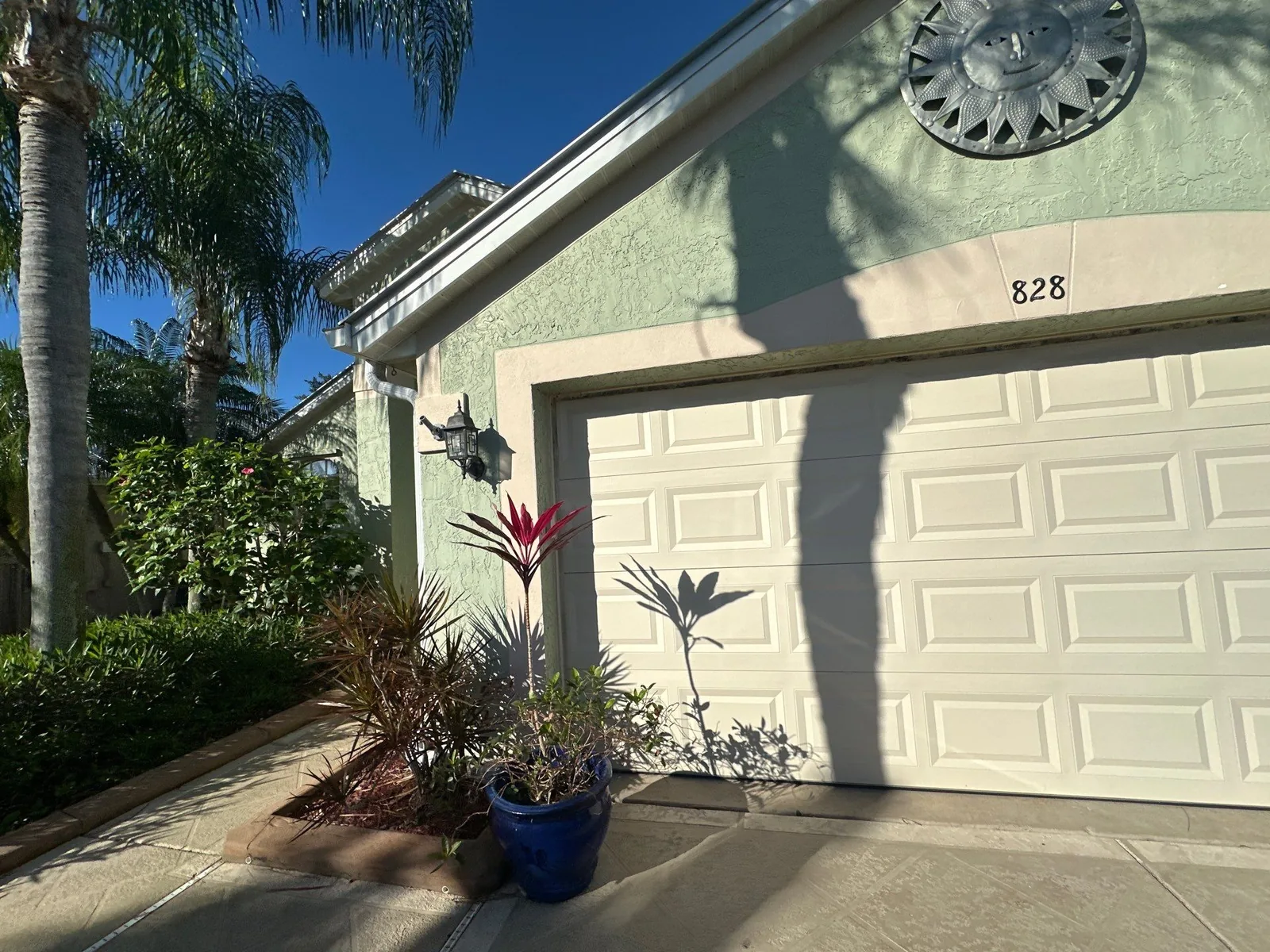 Exterior Painting in North River Shores, Florida. Single-storey stucco home exterior painted pale green with white garage door and white trim, palm trees at left.
