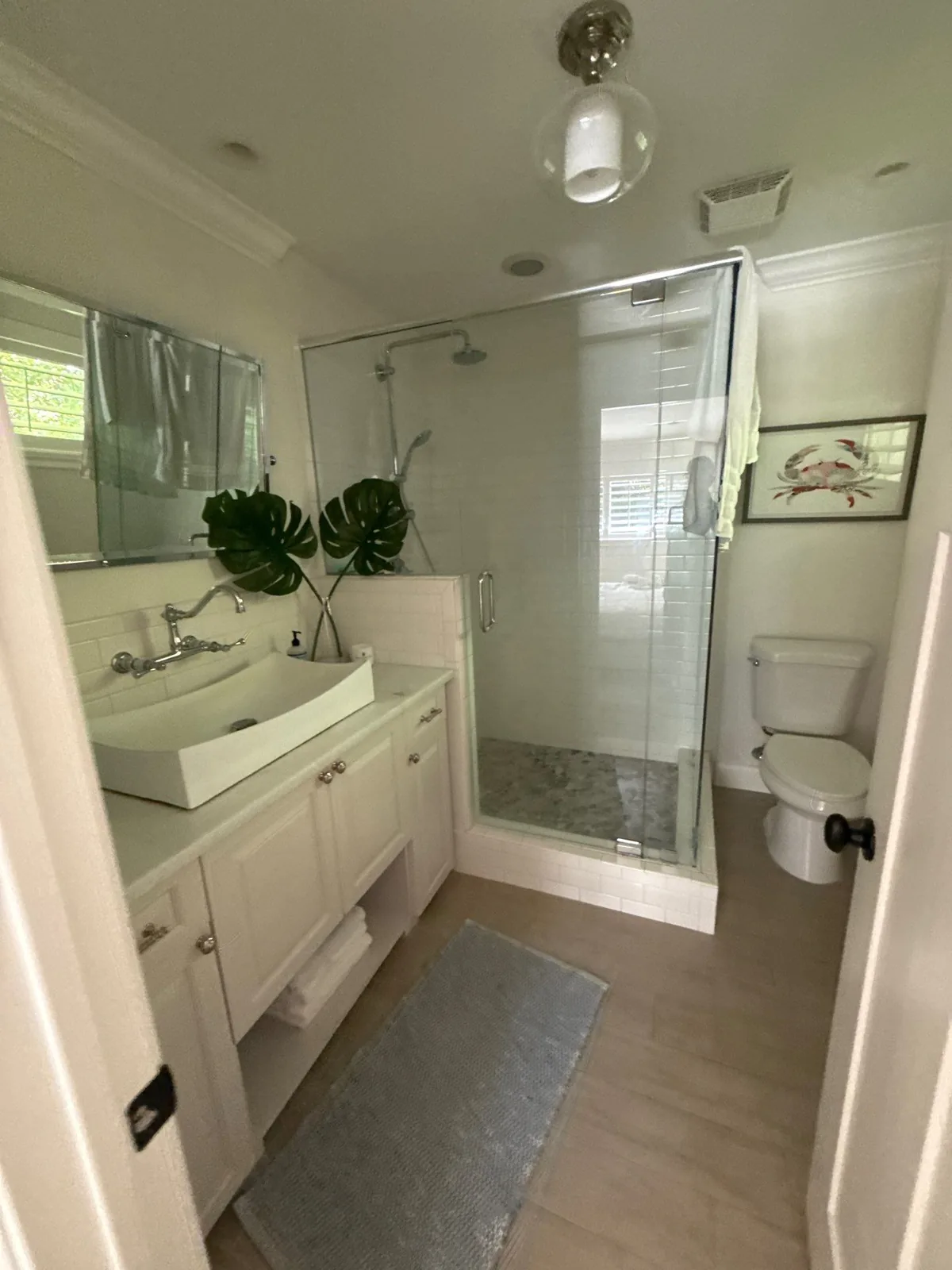 Interior Painting in North River Shores, Florida. Bathroom with light walls and crown moulding, white painted vanity cabinets, glass shower enclosure and toilet.
