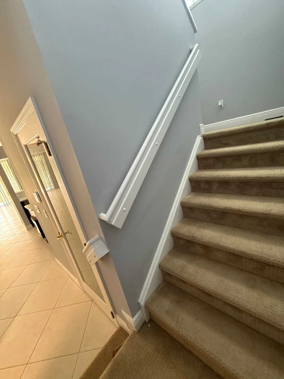 Interior Painting in North River Shores, Florida. Interior stairway with grey-blue walls, white painted handrail, baseboard and door casing, and carpeted stairs.