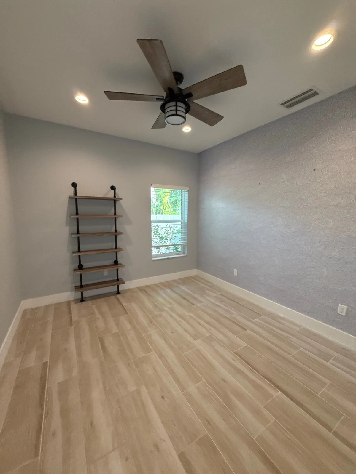 Interior Painting in North River Shores, Florida. Empty bedroom with pale grey walls, white baseboard and window trim, ceiling fan and light wood-look tile floor.